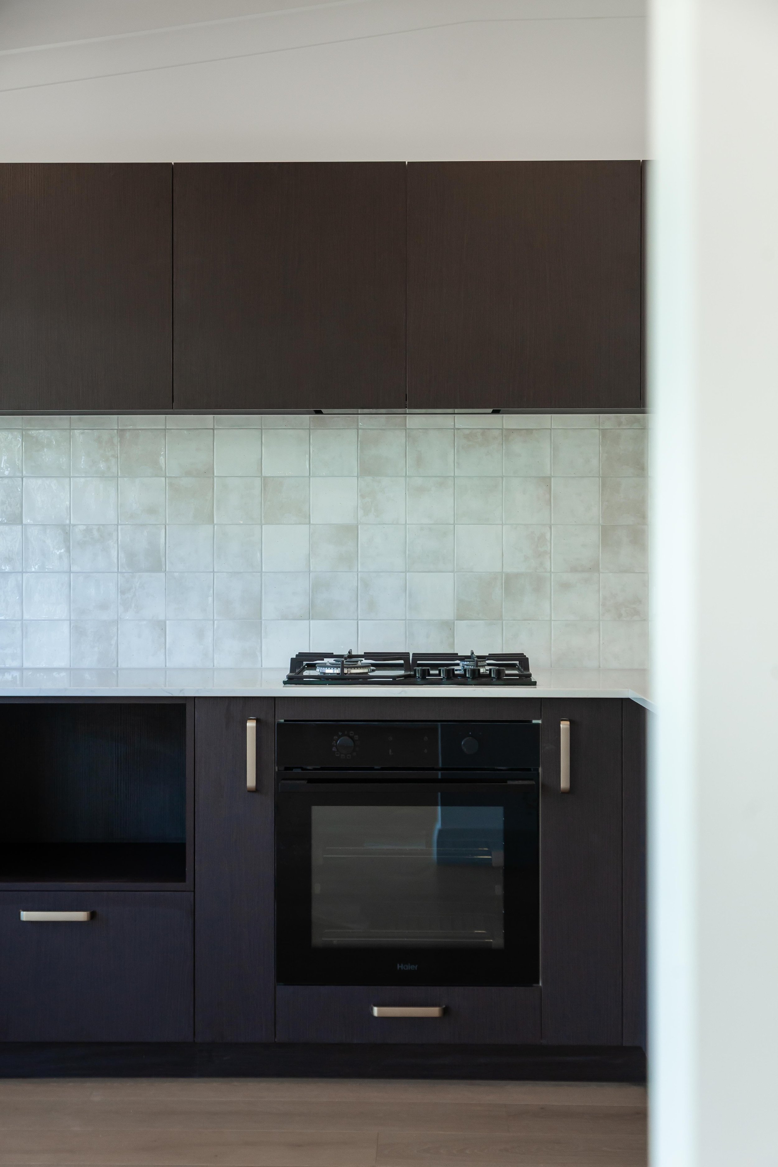 Modern kitchen with dark wood cabinets, a black oven, and a tiled backsplash.