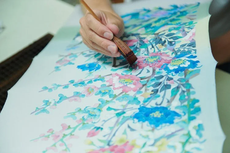Close-up of a hand painting colorful floral patterns with a brush on paper.