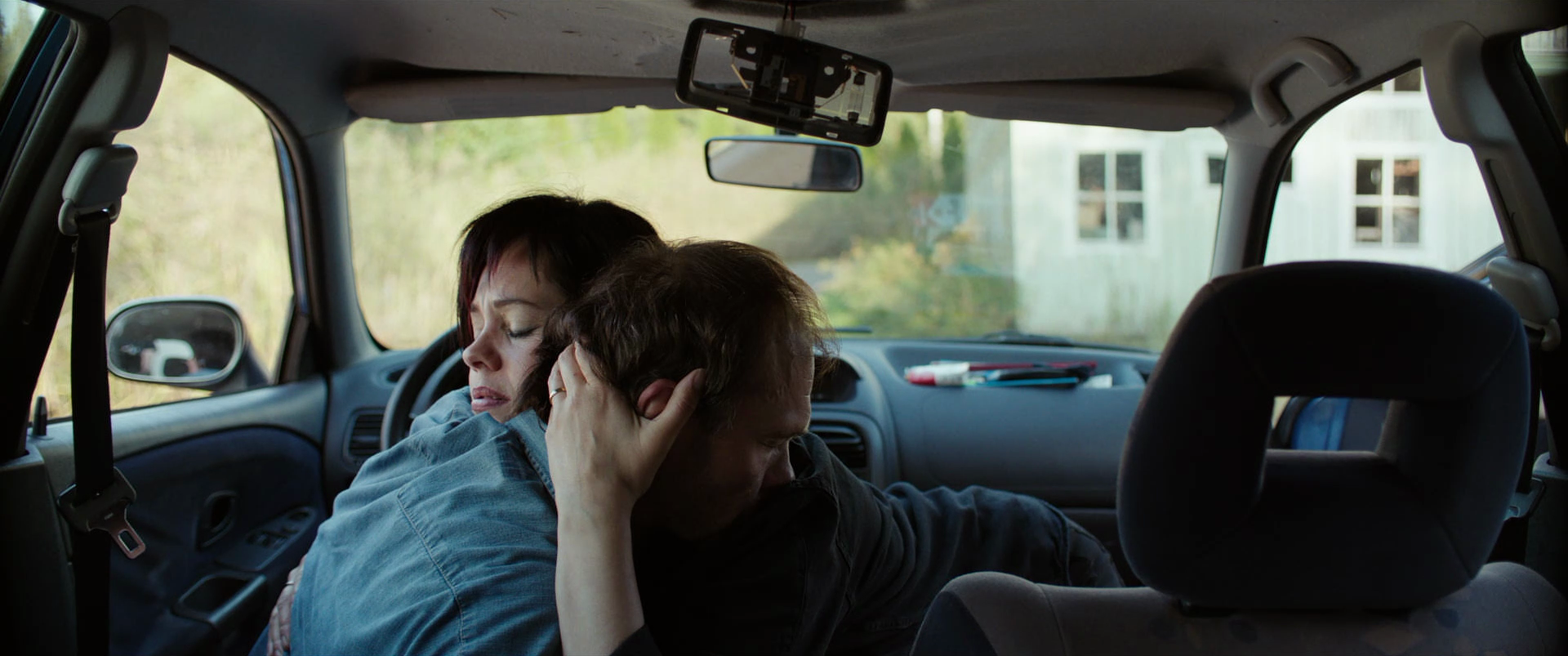 A woman and a man are hugging each other inside a vehicle, with the woman holding the man's head and both appearing emotional.