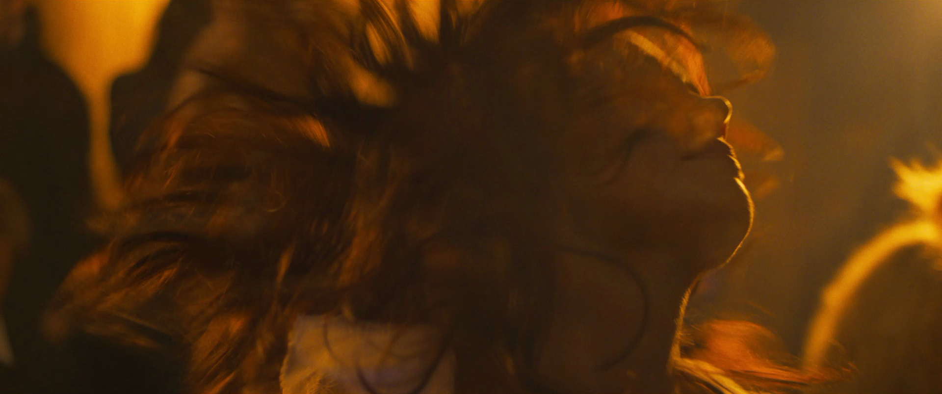 Close-up of a woman with wavy hair illuminated by warm golden light, with her head tilted back and eyes closed.