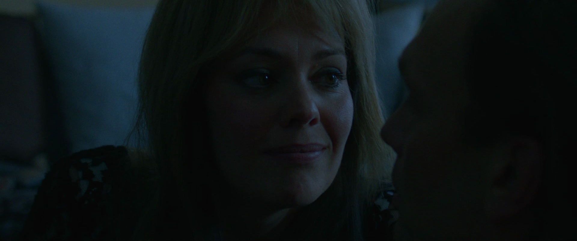 Close-up of a woman with blonde hair looking at a man in a dimly lit setting.