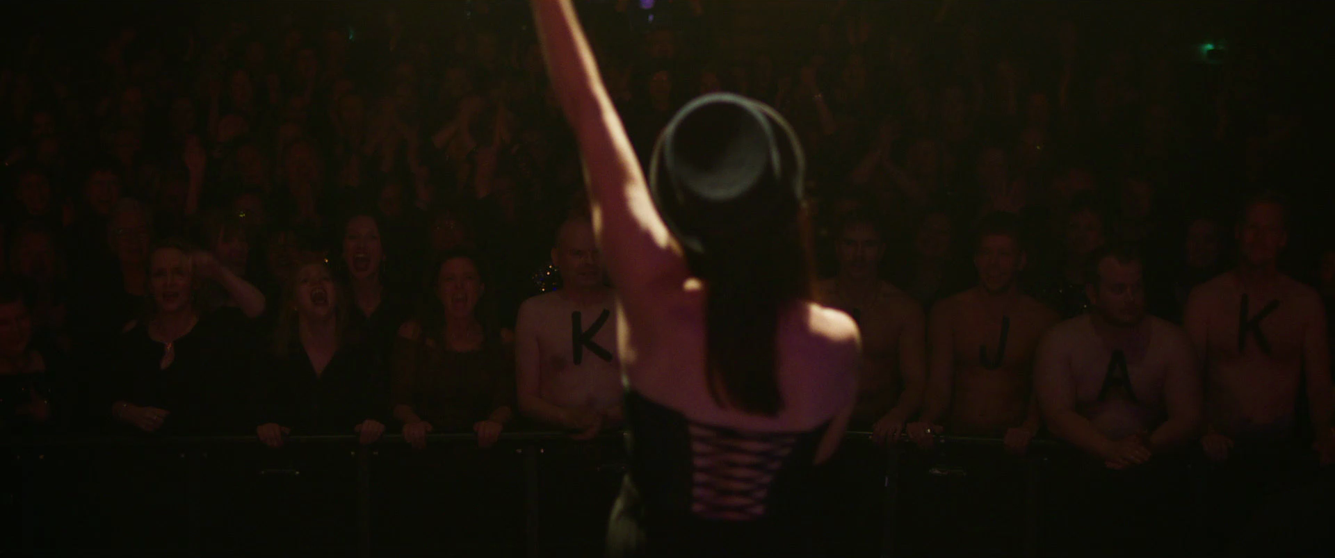 A woman performing a pole dance on stage in front of a cheering audience.