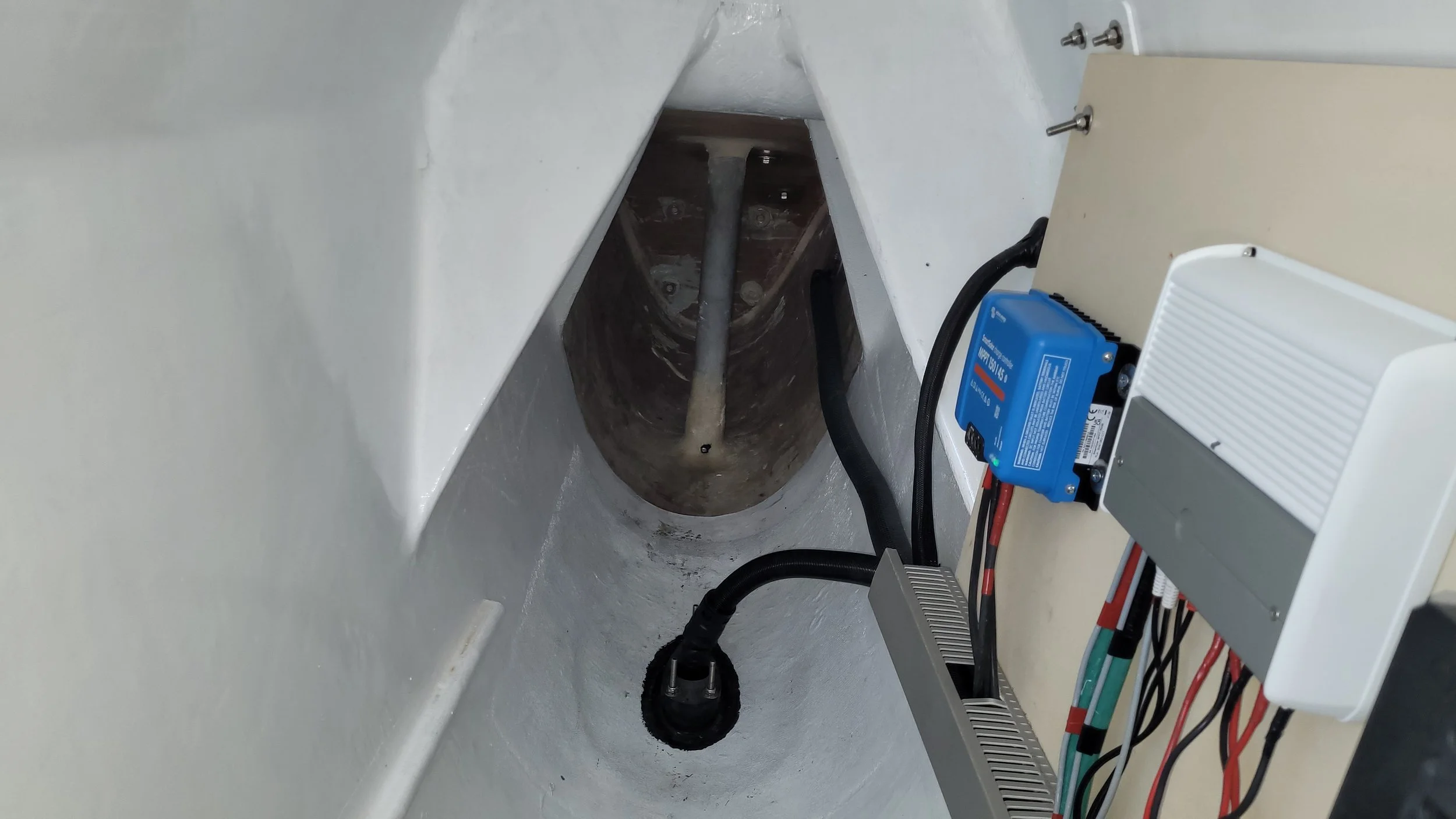 Inside a hull with electronic control devices mounted, MPPT, on the wall, including a blue device and a white box with wires, with a metal rod or pipe visible at the far end.
