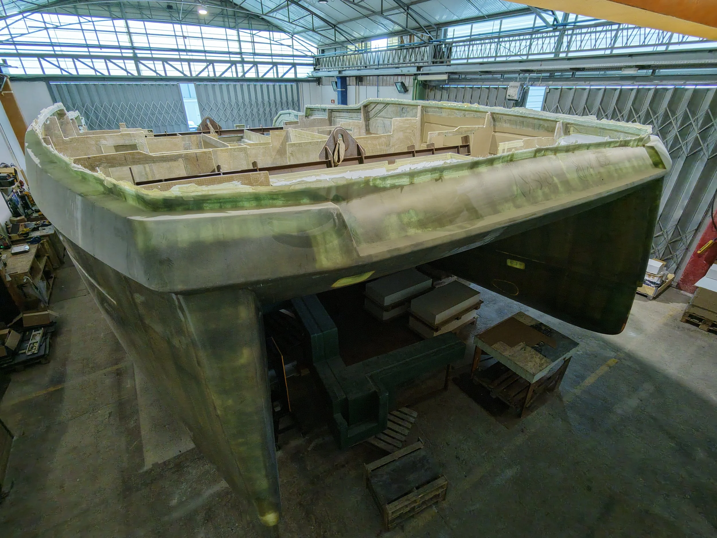 A large boat under construction inside a spacious workshop, with scaffolding and tools around.