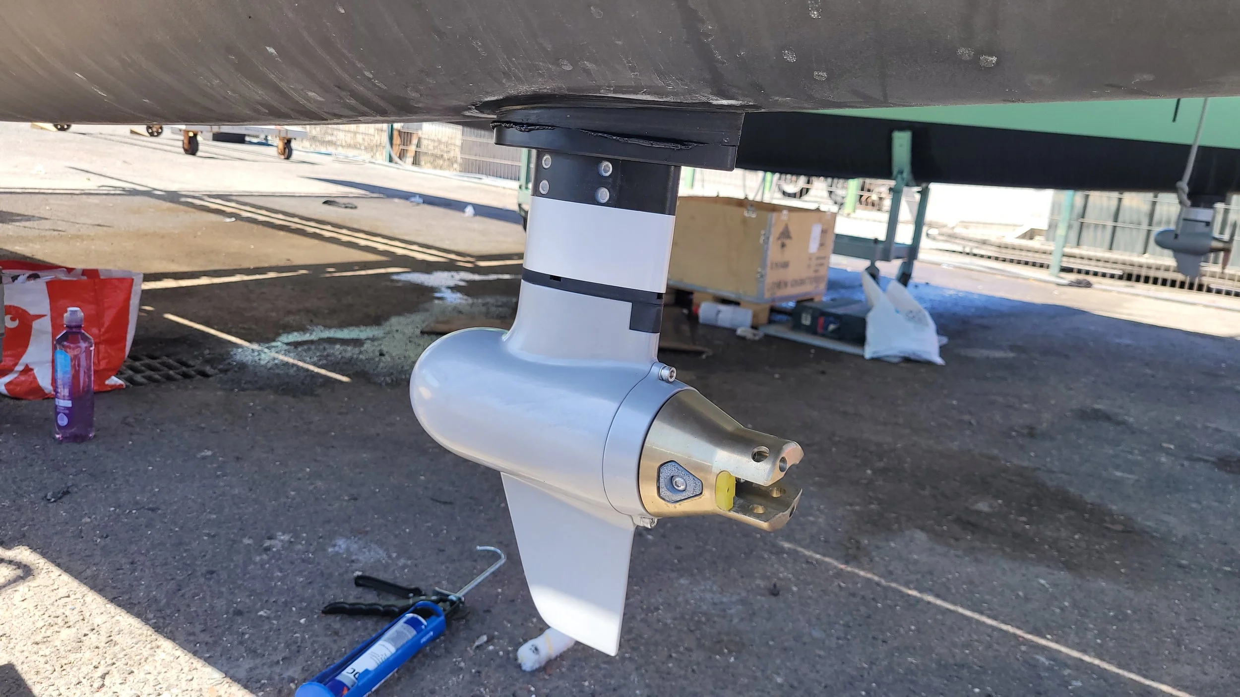 Close-up of an electric boat motor attached to the stern of a boat, with tools and supplies scattered on the ground nearby outside.
