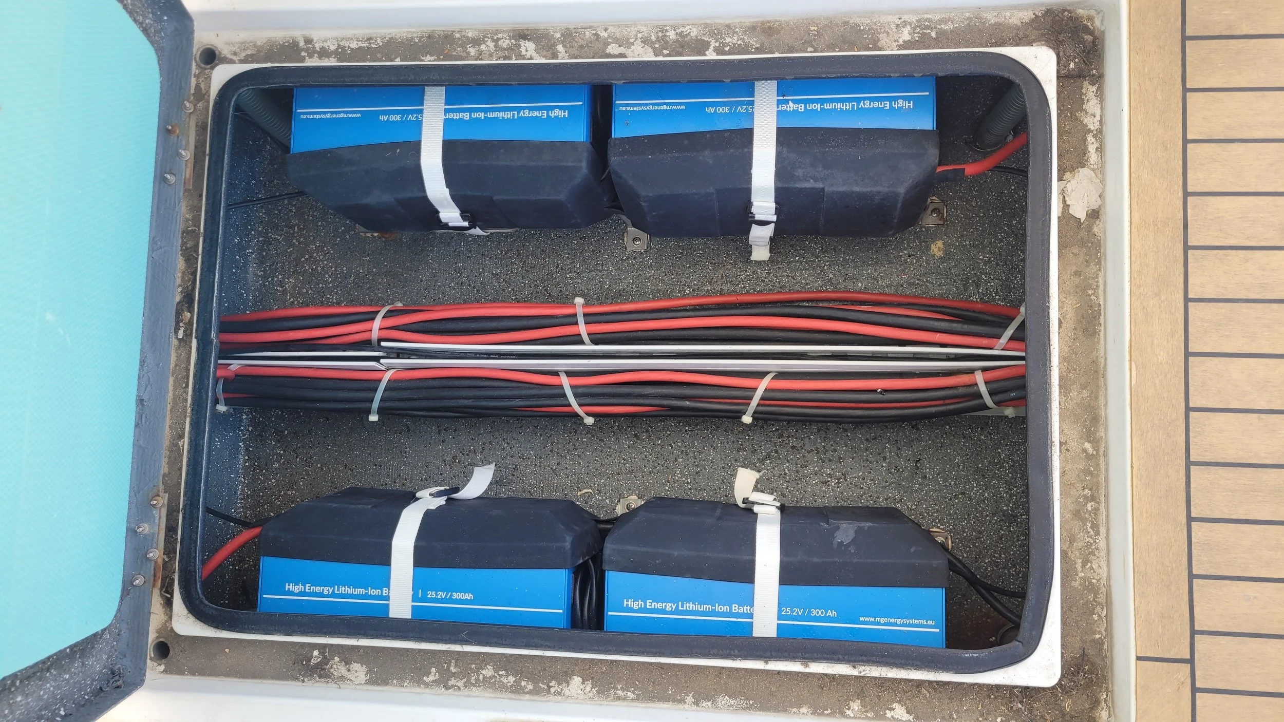 Four lithium-ion batteries and multiple red and black cables organized with zip ties inside an enclosure.