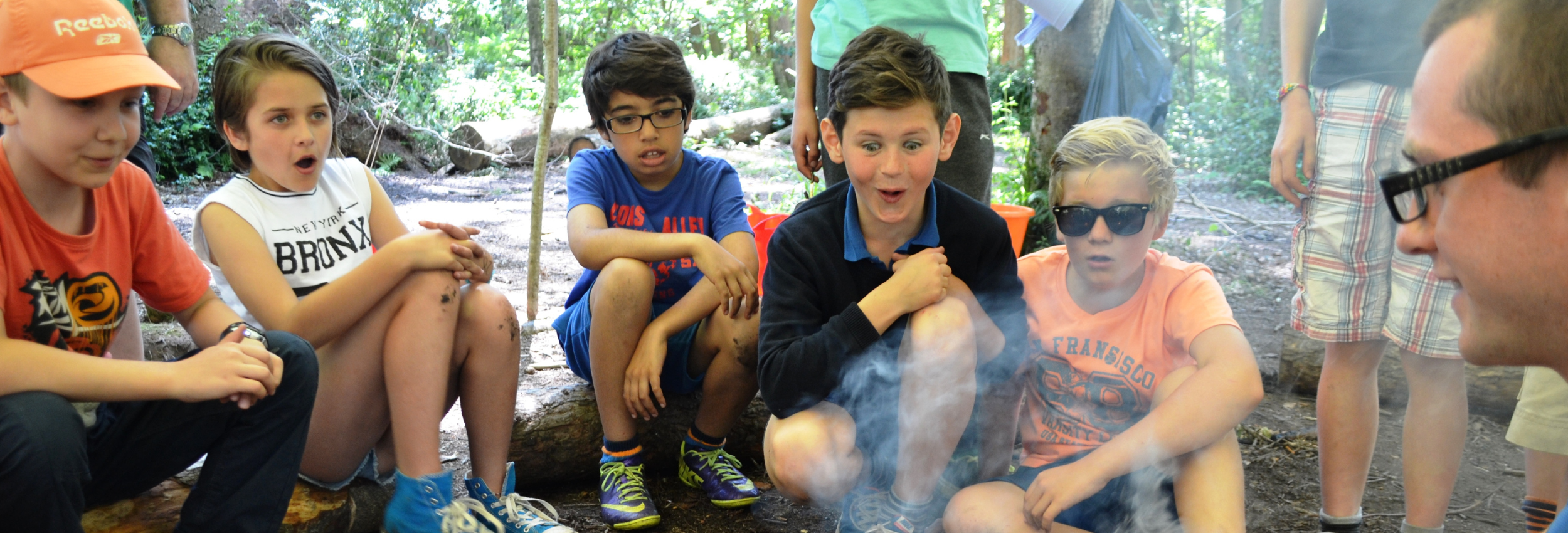 Image shows a group of older primary school children enjoying a campfire on a school trip. Their faces show amazement as the fire is lit