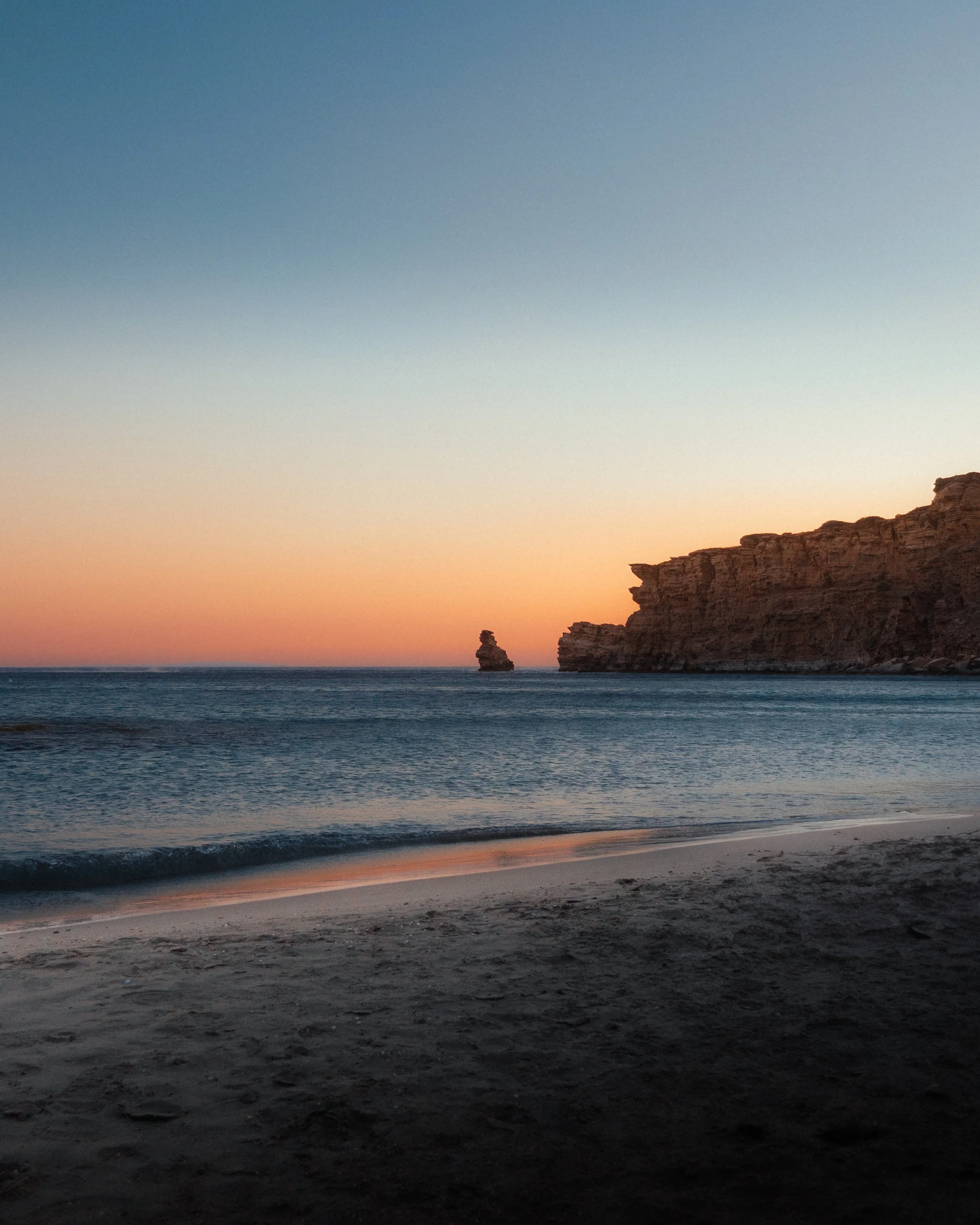 Cliffs and a quiet beach beneath a colourful sunset sky.