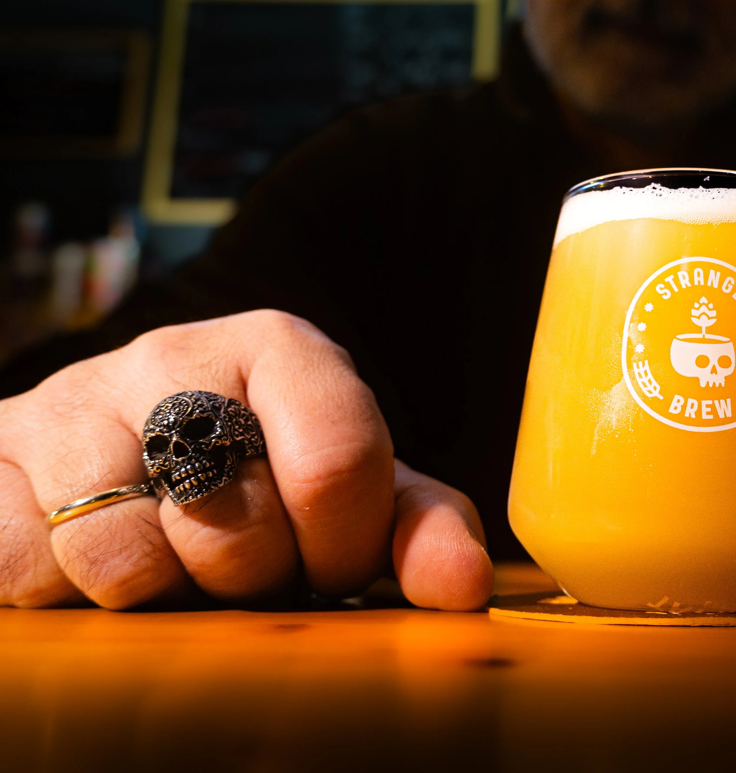 A ringed hand beside a glass of hazy beer on the bar.