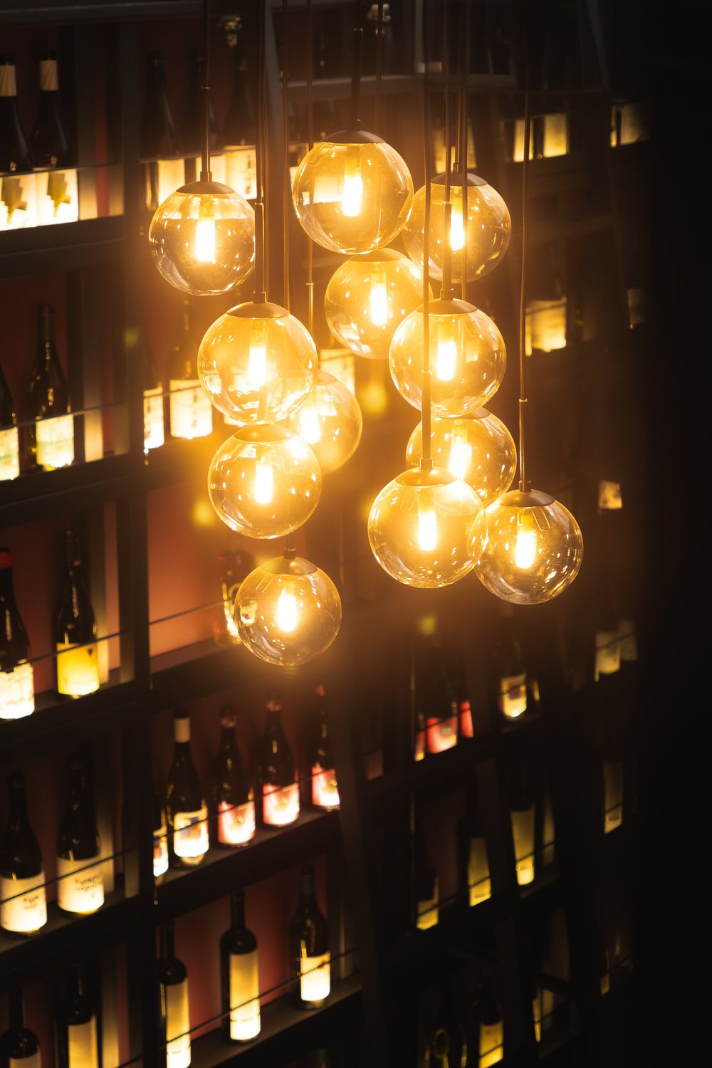A cluster of glowing pendant bulbs beside wine bottles at Strafilo.