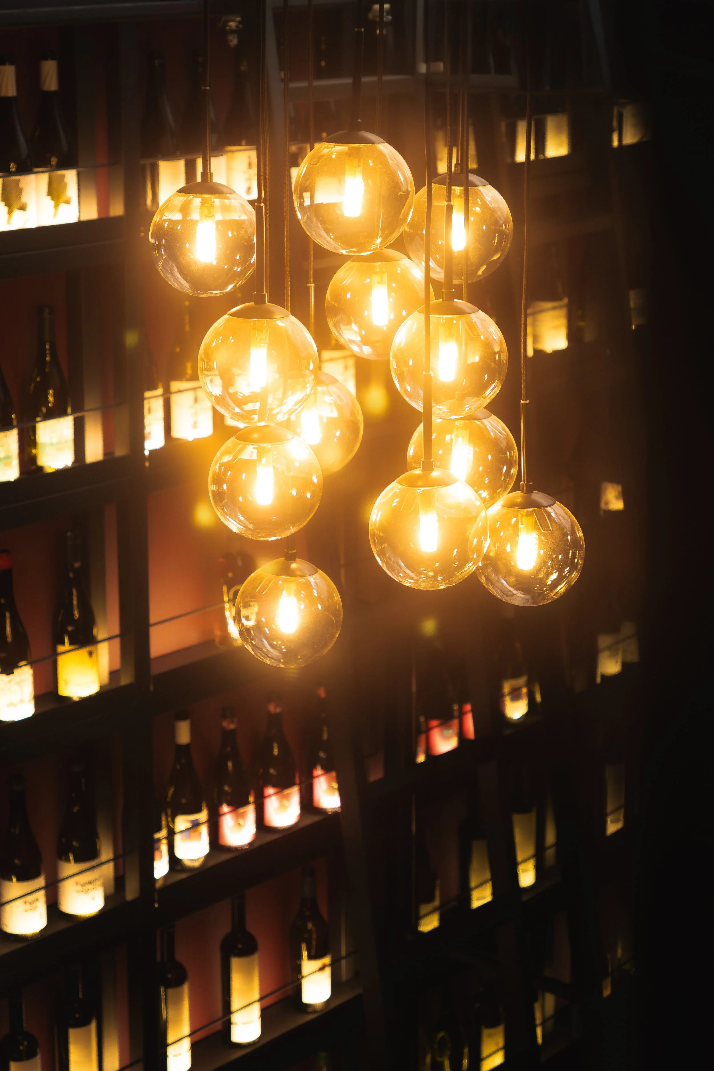 A cluster of glowing pendant bulbs beside wine bottles at Strafilo.