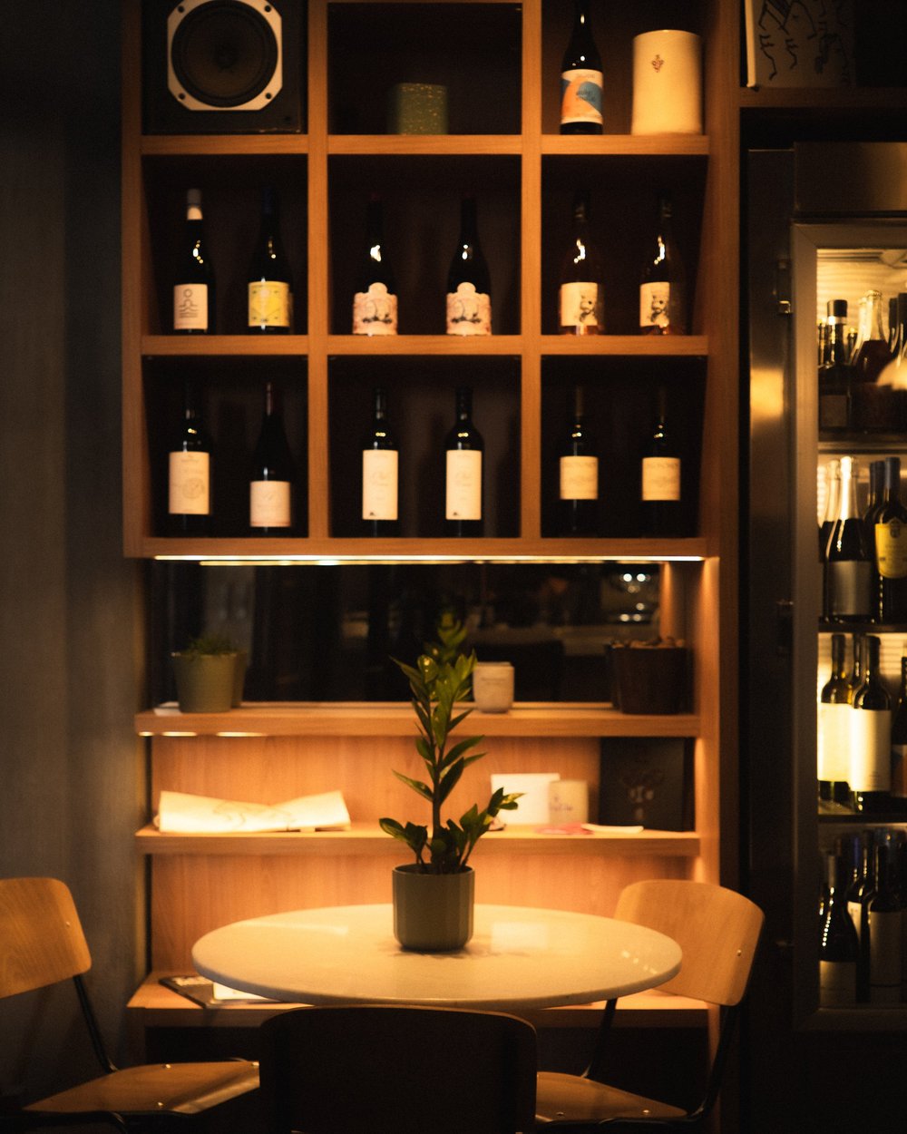 A small table beneath shelves of wine and a speaker at Strafilo.