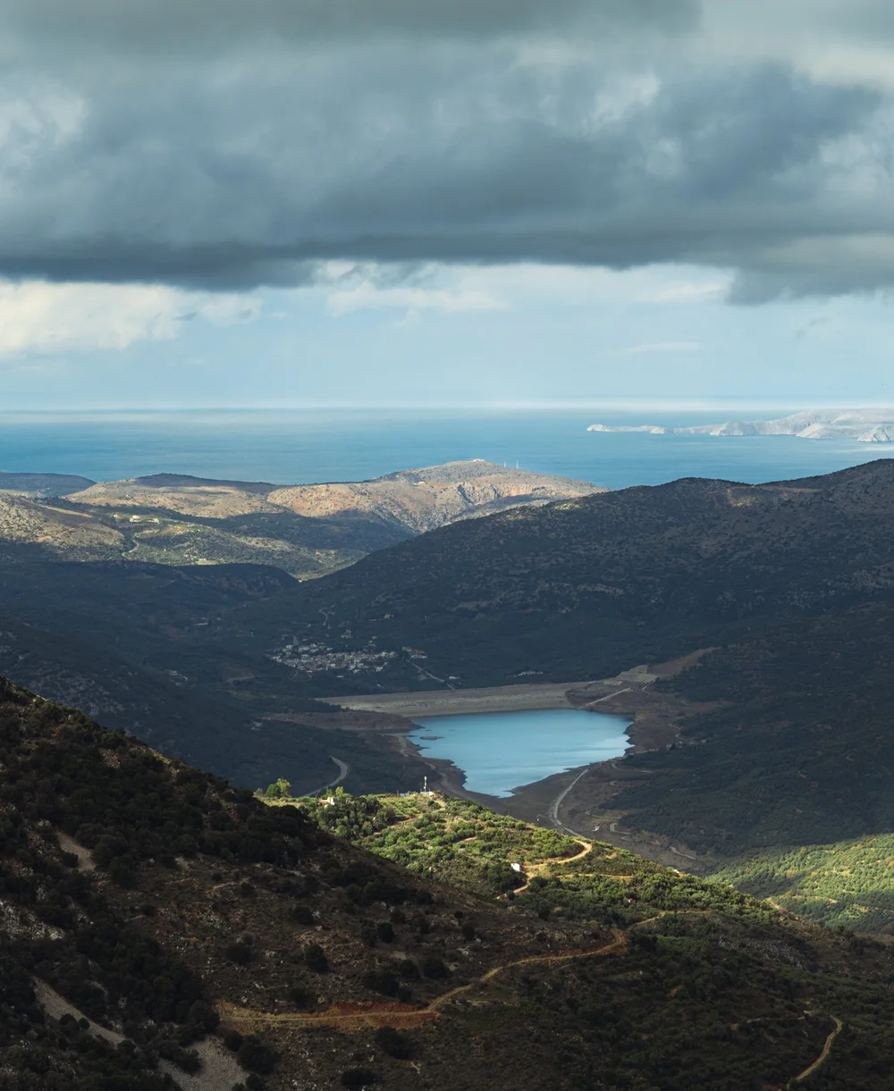 A mountain panorama with a lake in the valley beneath a cloudy sky.