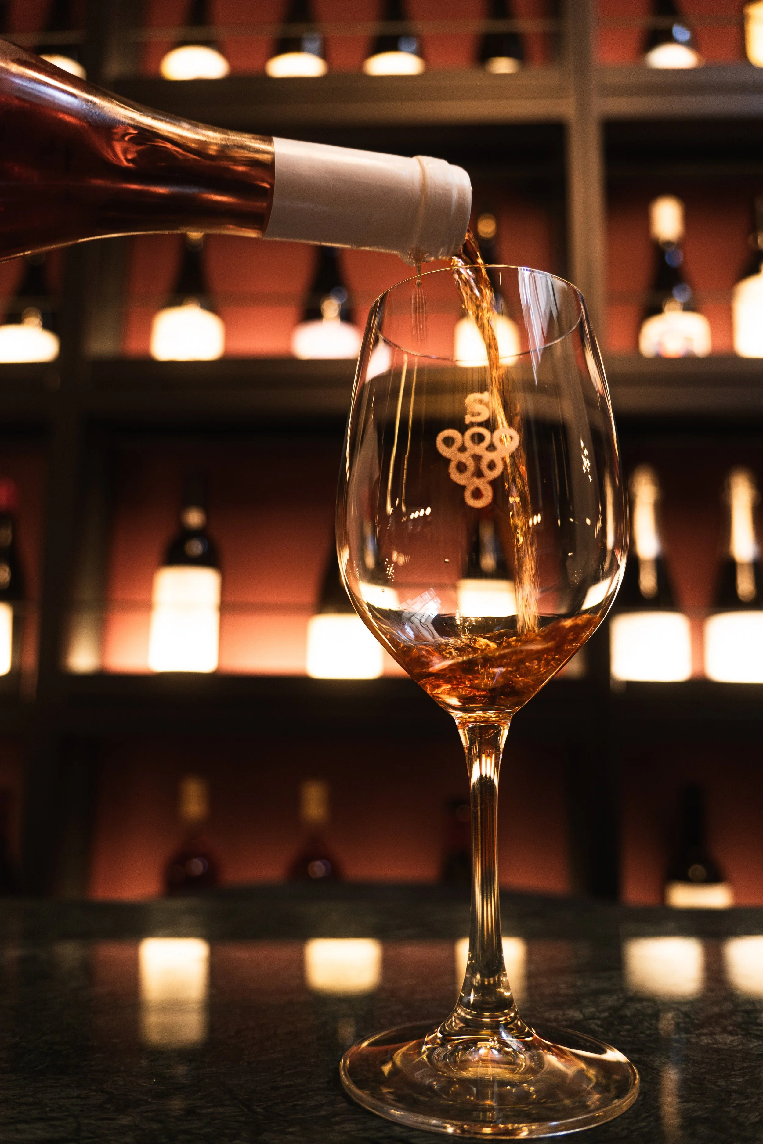 An empty wine glass in front of illuminated bottle shelves.
