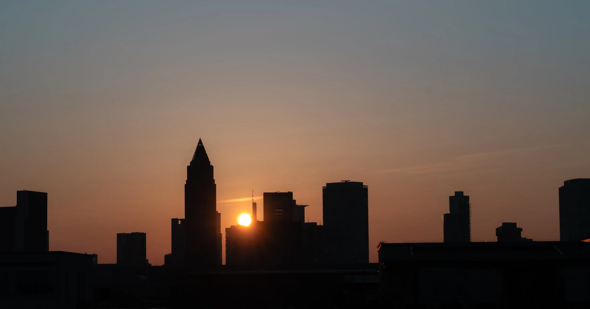 Sun setting behind the silhouette of a city skyline with tall buildings during dusk.