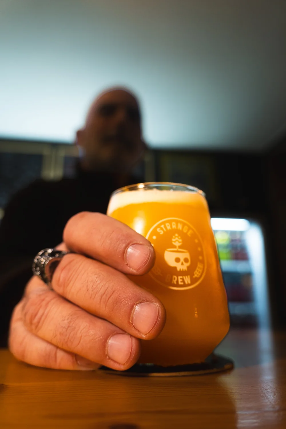 A hand holding a glass of beer across the bar.