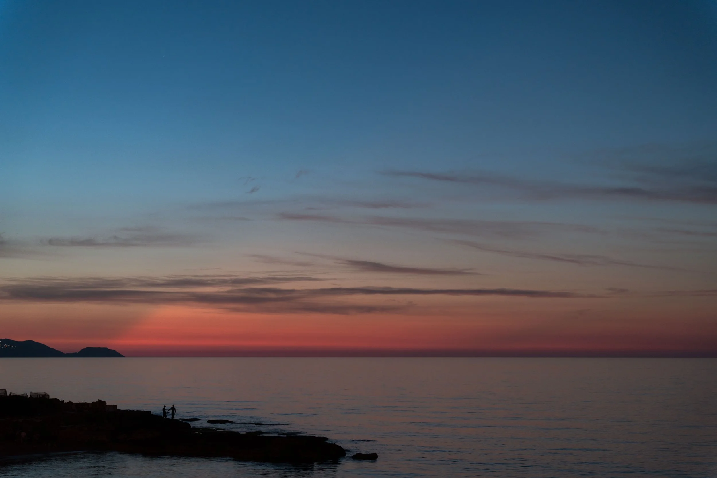 Rocky shoreline and distant islands under a blue and pink sunset sky.