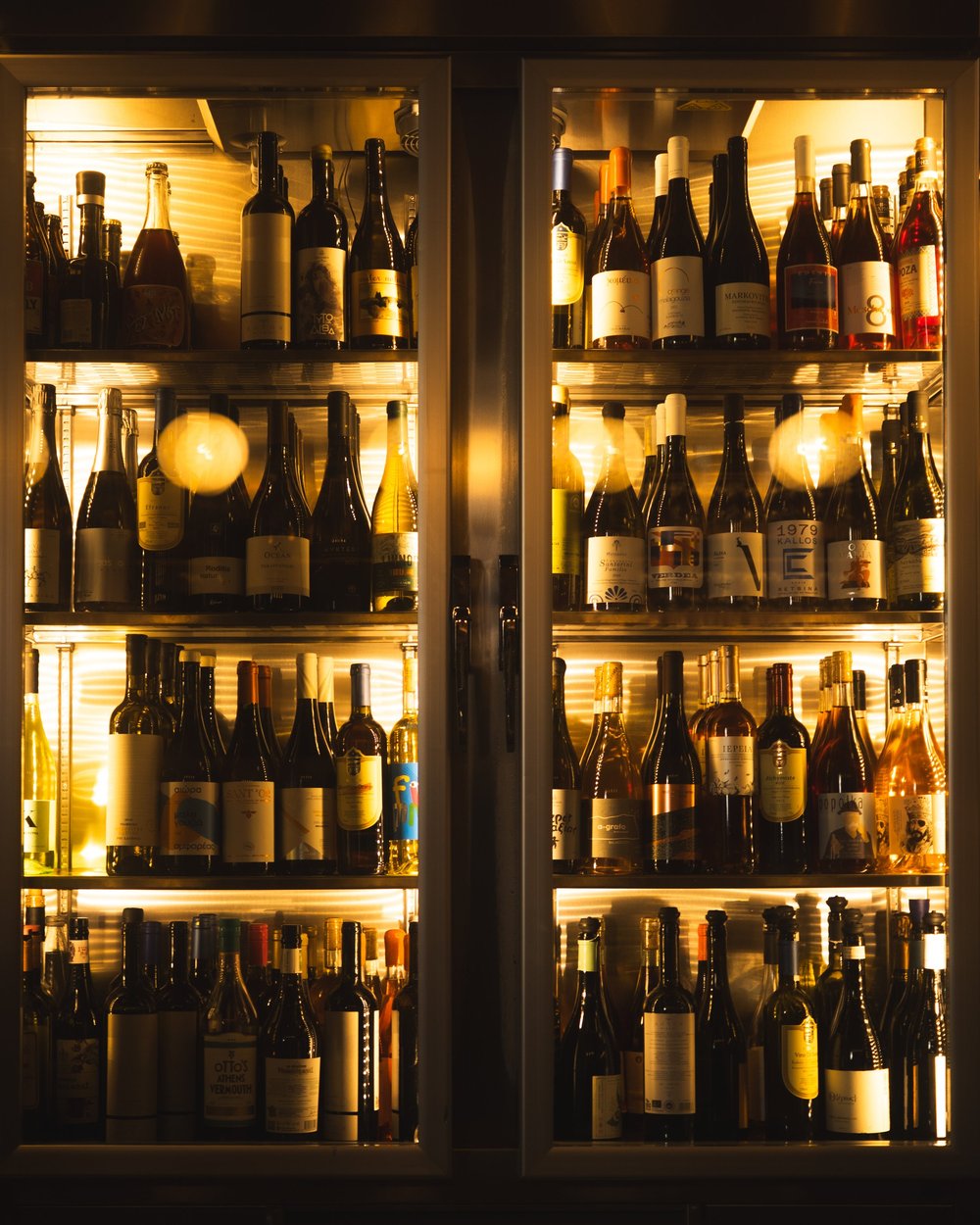 Rows of wine bottles inside a lit glass-fronted cabinet at Strafilo.