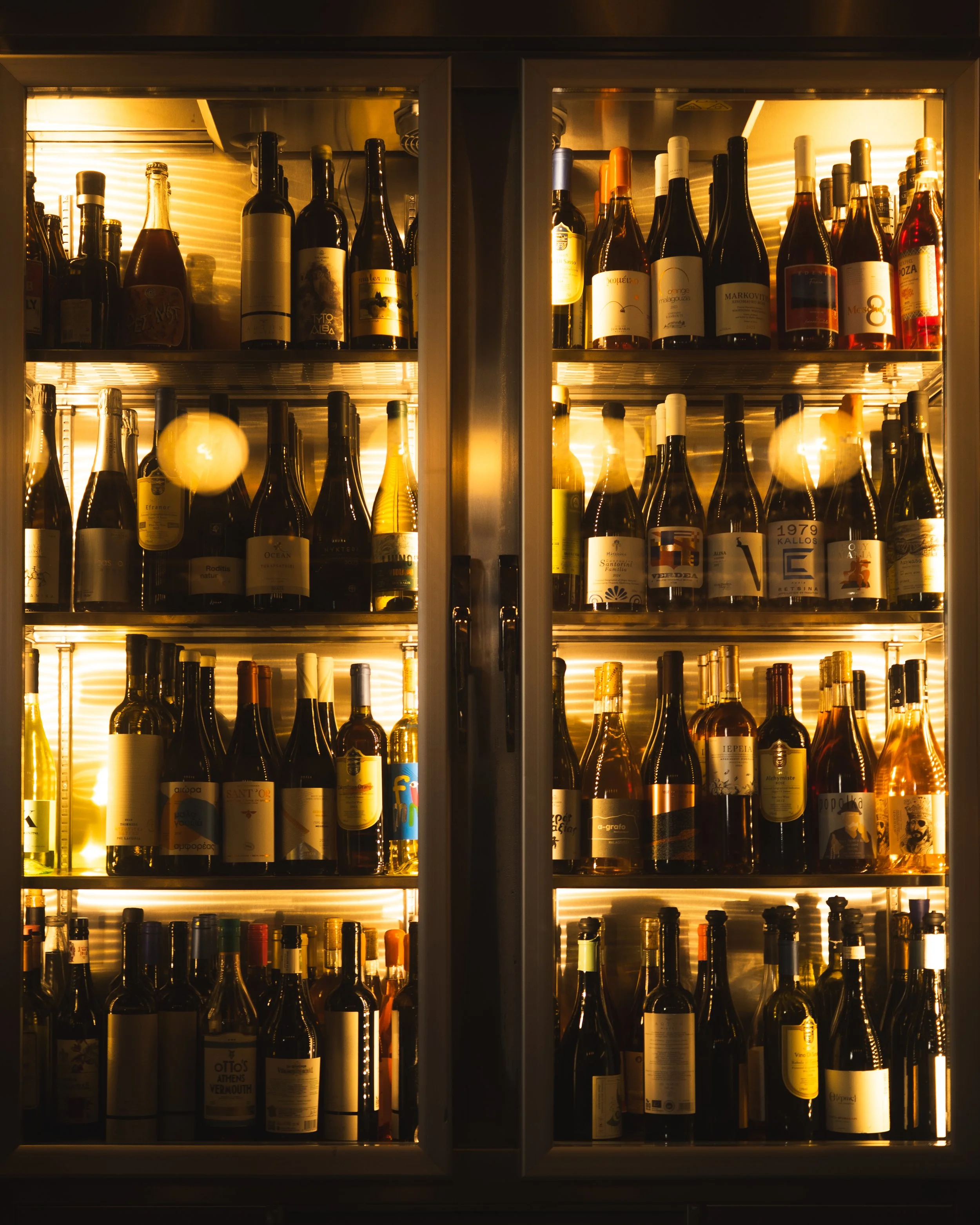 Rows of wine bottles inside a lit glass-fronted cabinet at Strafilo.