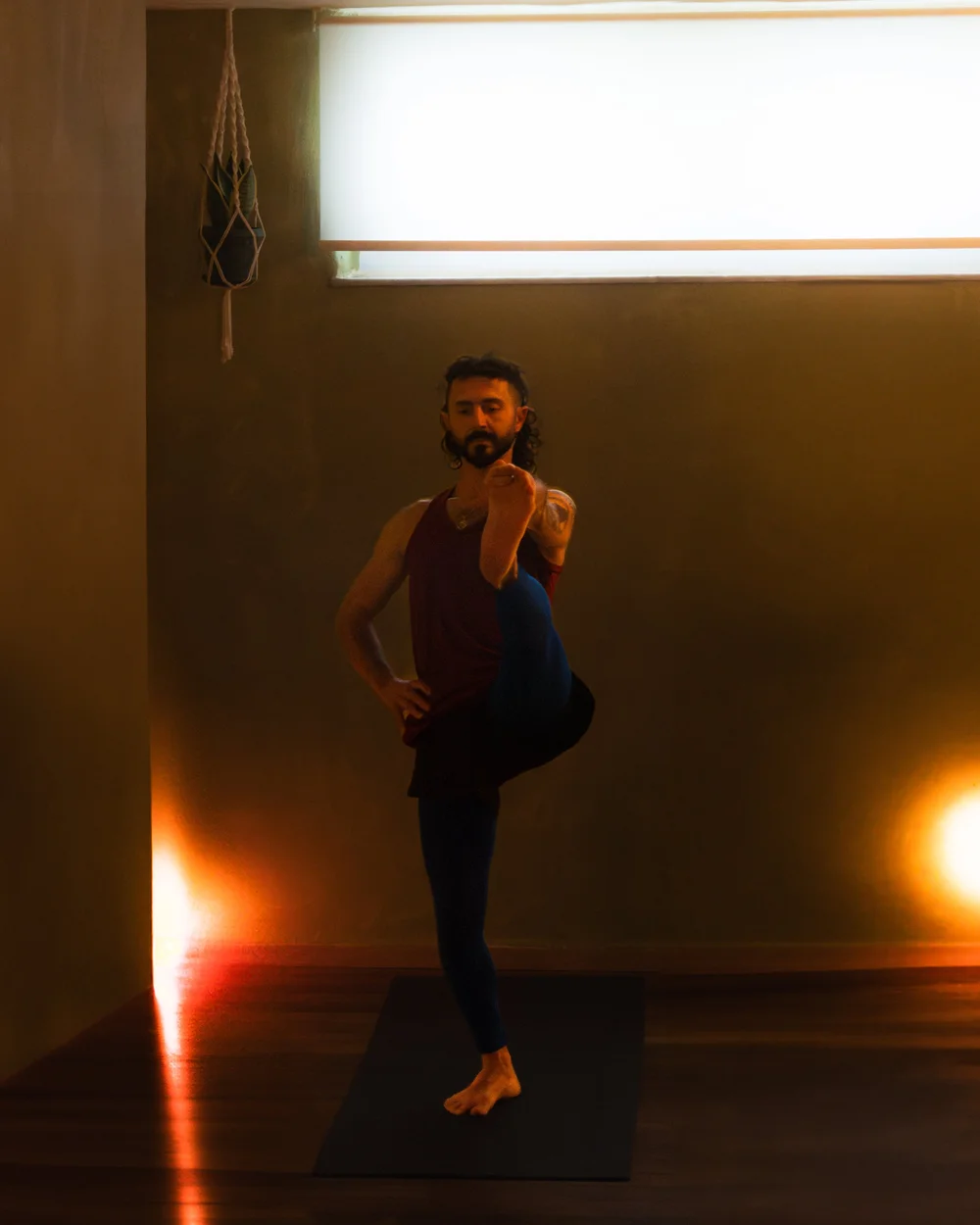 A yoga participant balancing upright beside a warm floor light.