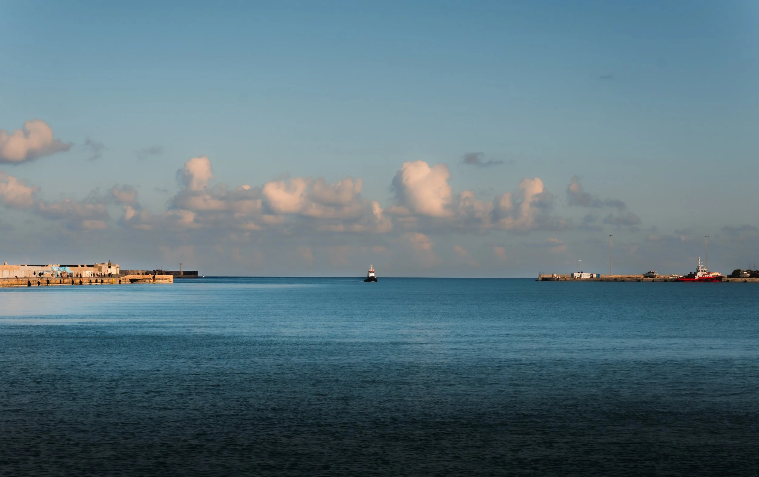 Blue harbour water between two breakwaters, with a lighthouse in the distance.
