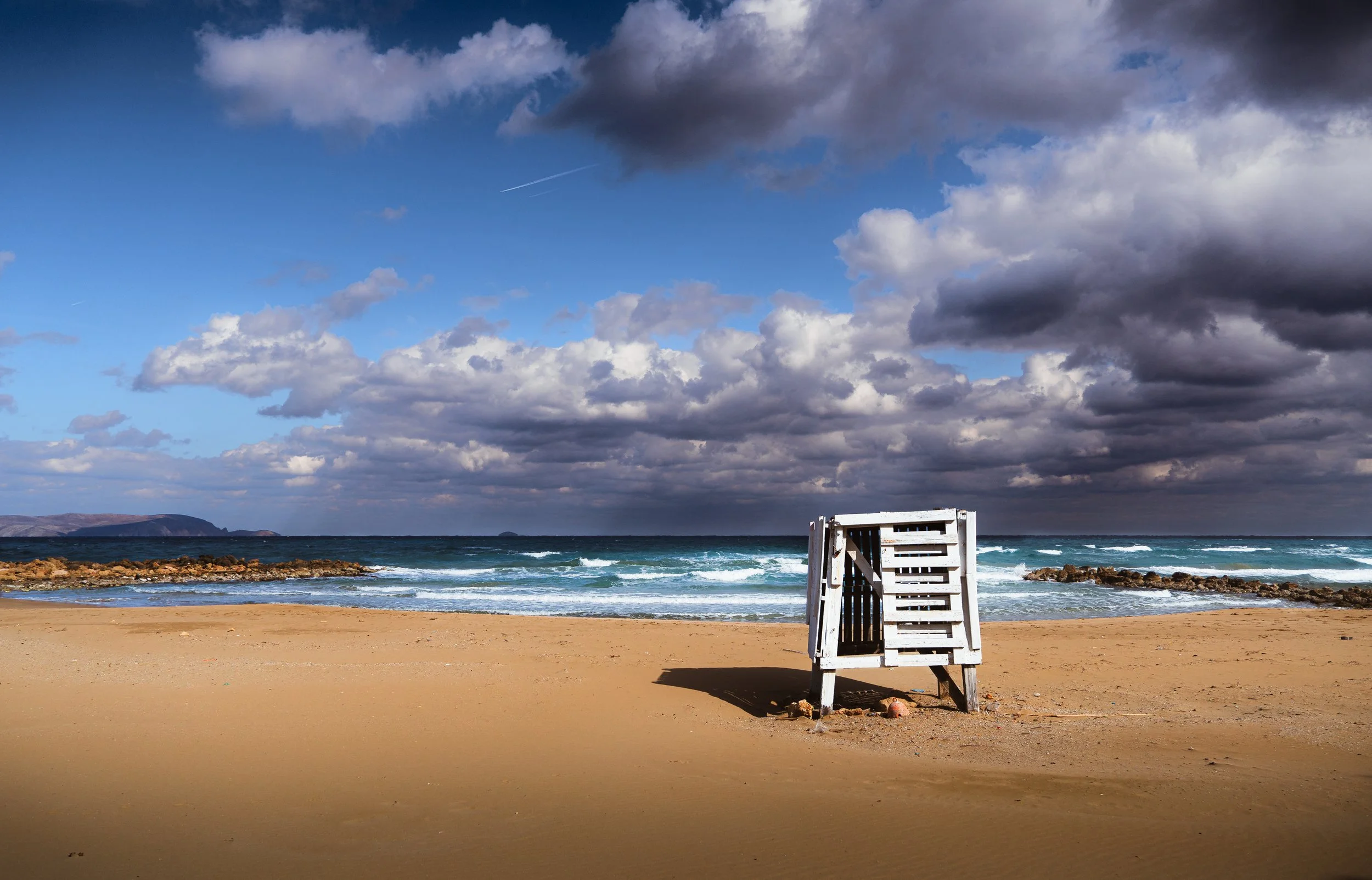 An empty lifeguard stand on a sandy beach beneath a cloudy sky.