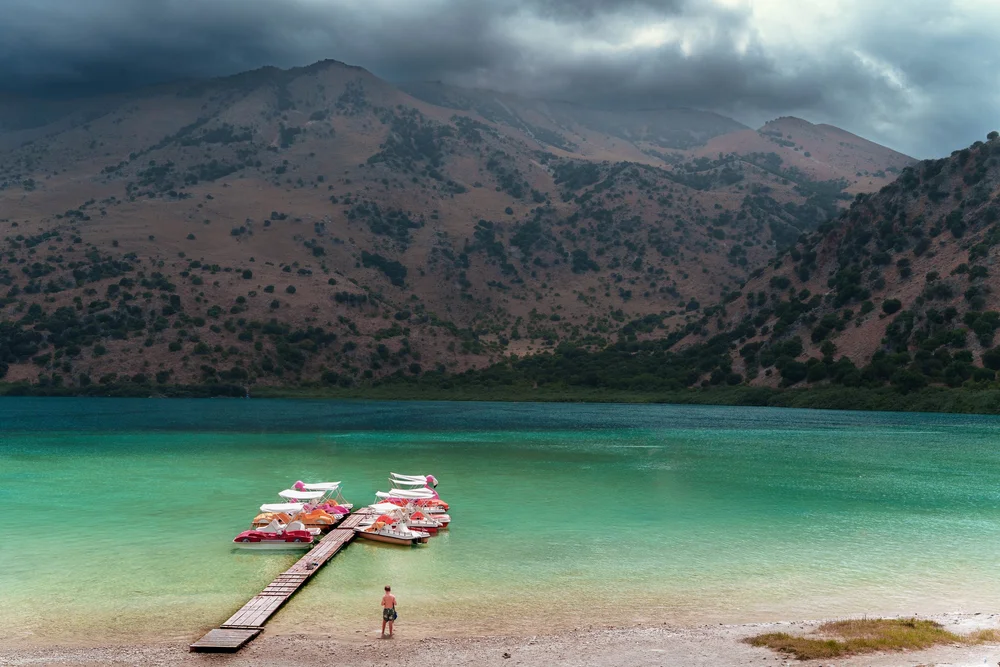 Boats beside a wooden jetty on a turquoise mountain lake beneath low cloud.