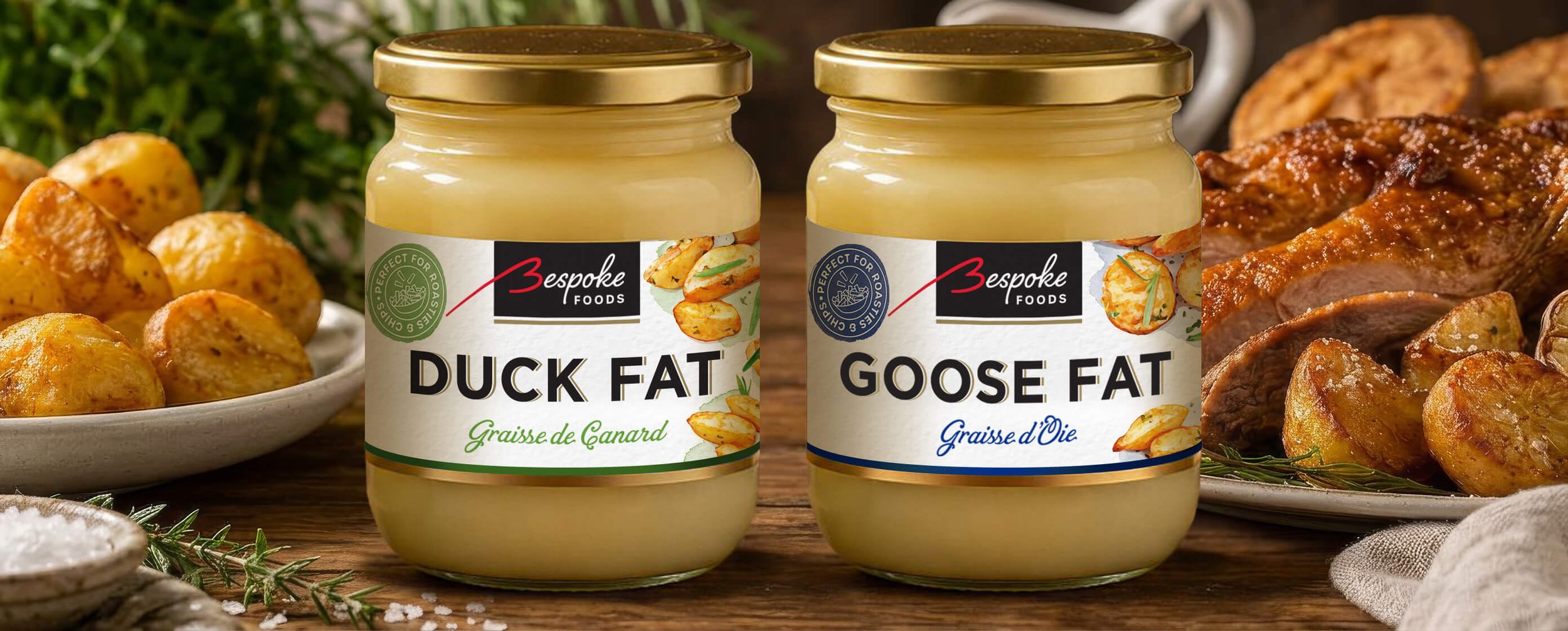 Two jars of duck fat and goose fat by Bespoke Foods placed on a wooden surface, surrounded by roasted potatoes, cooked meat, and herbs.