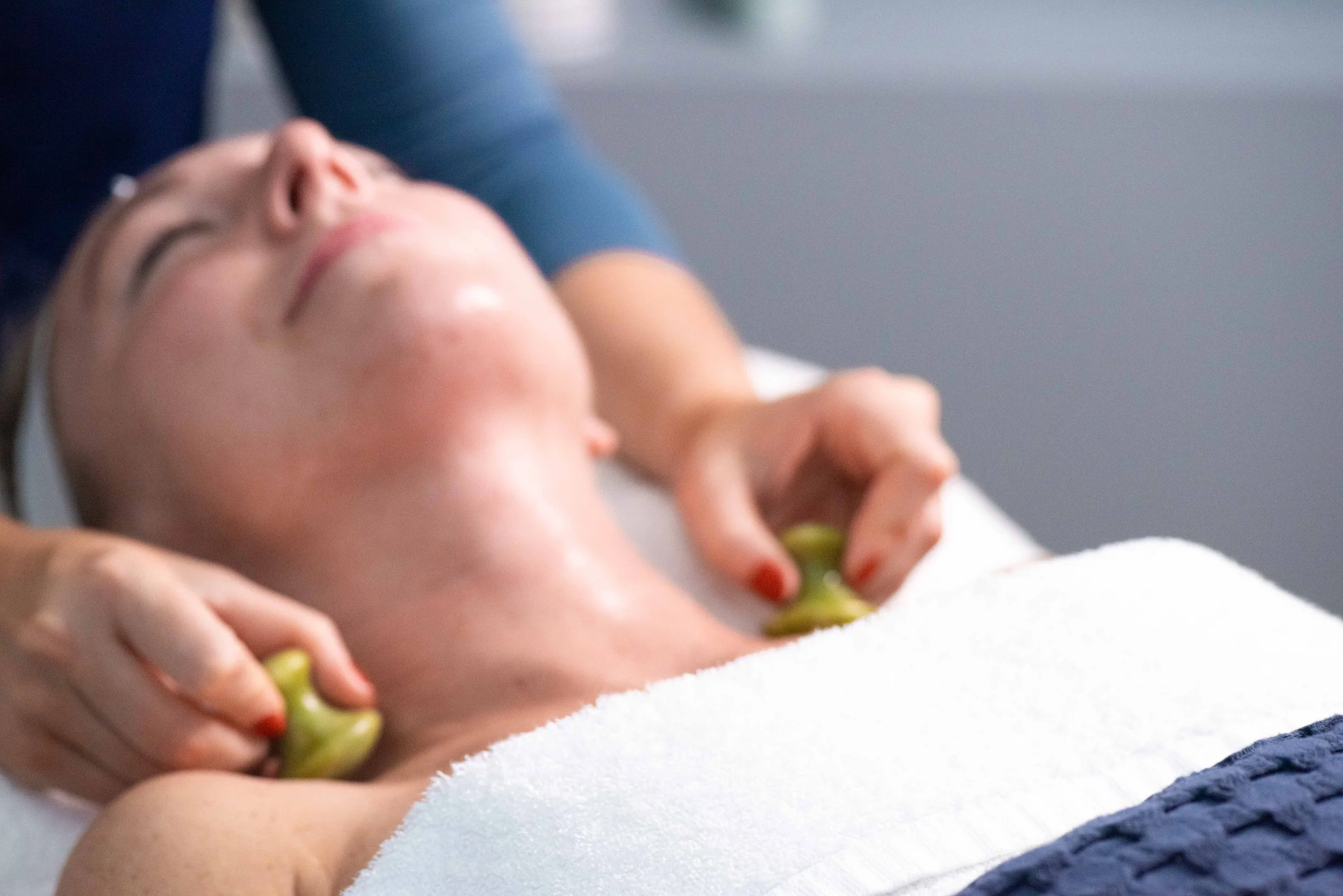 Close-up of a person receiving a massage with jade stones on their neck in a spa setting.