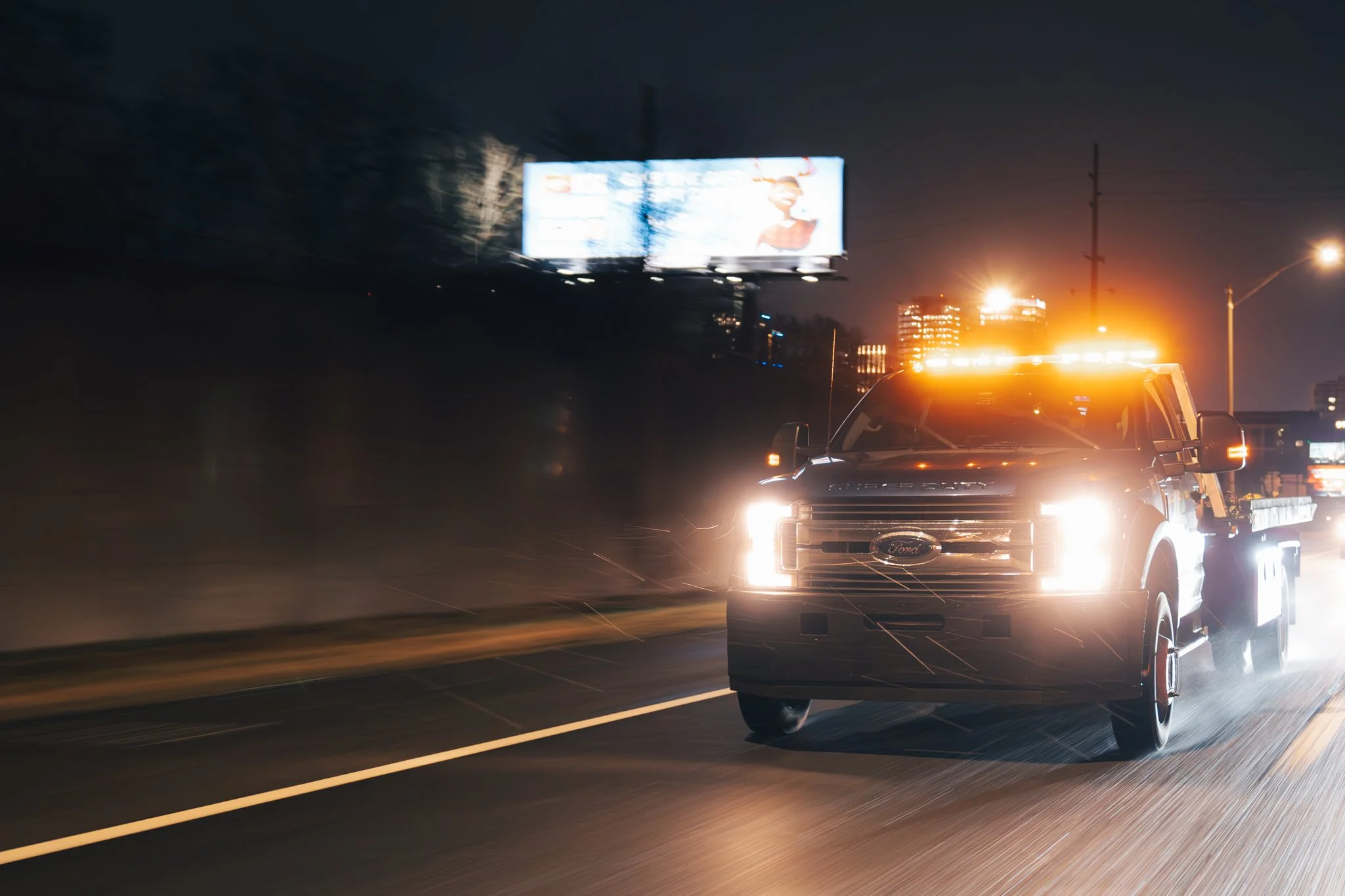 Tow truck with flashing lights driving on a highway at night.