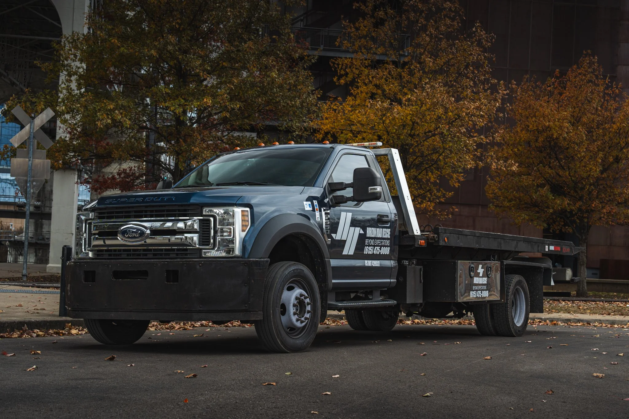 Ford Super Duty tow truck parked on a street with autumn trees in the background.