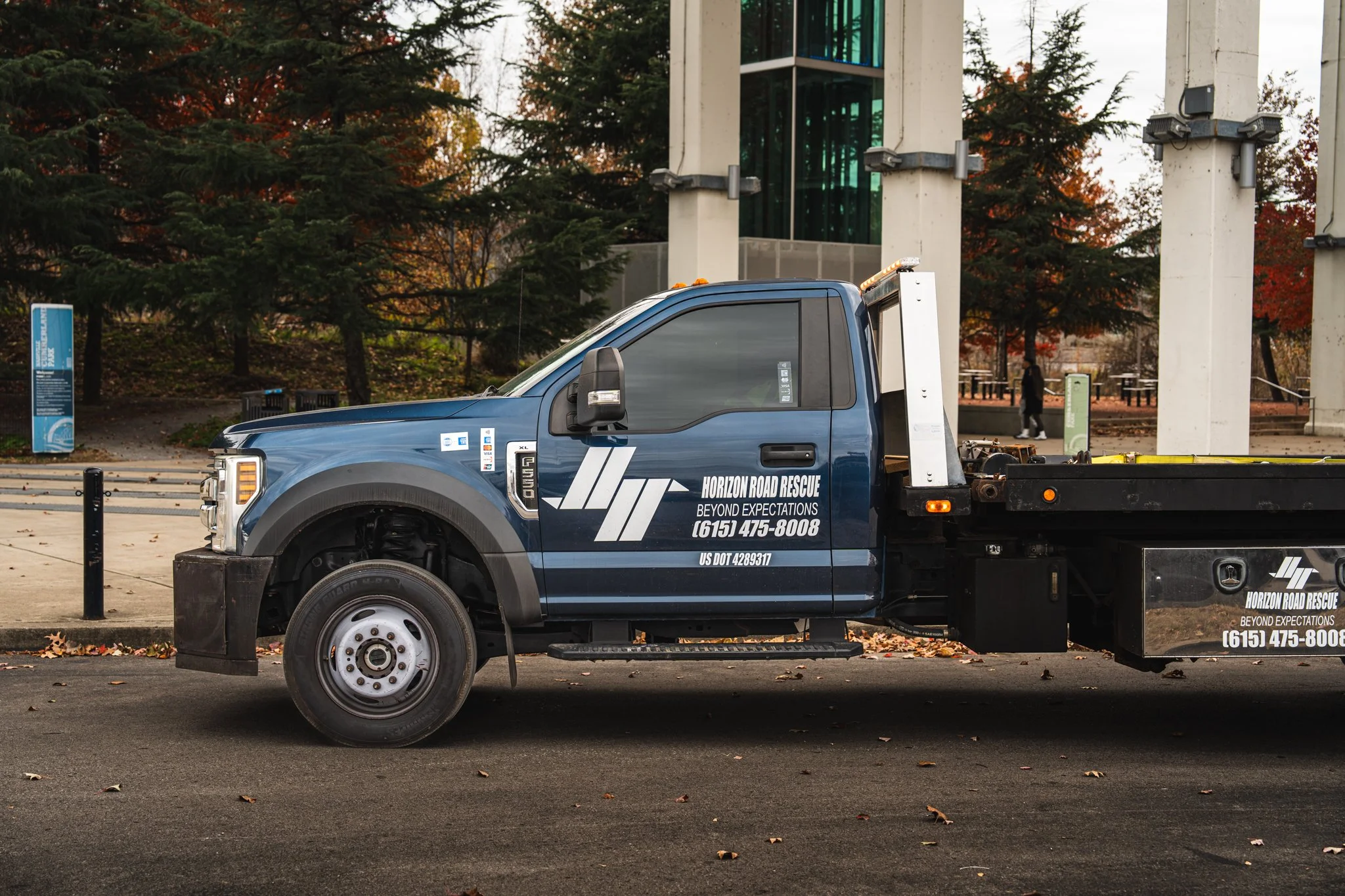 A blue tow truck with "Horizon Road Rescue" branding parked outdoors, near trees and large vertical structures.