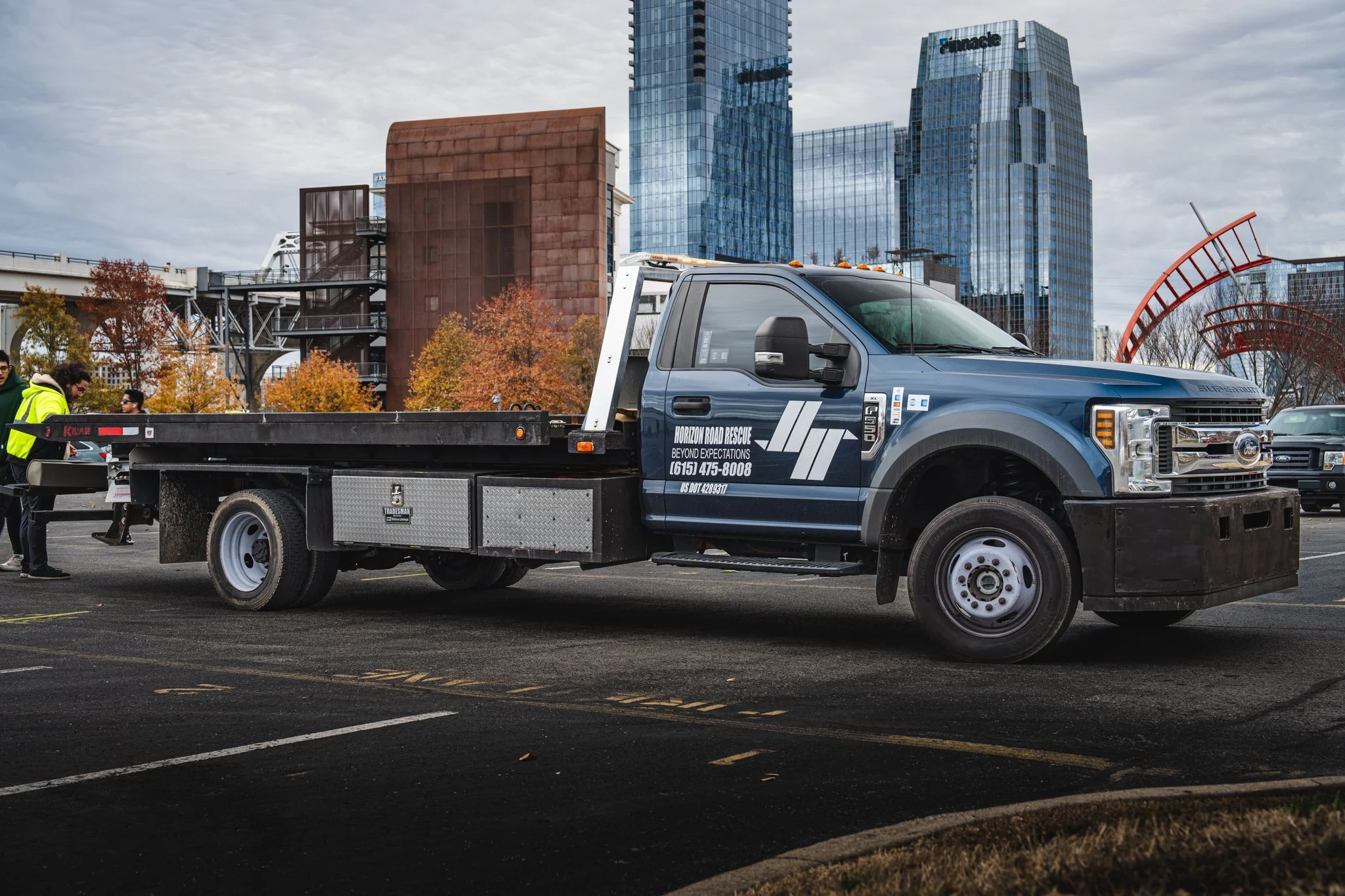Flatbed tow truck parked in an urban area in Nashville with skyscrapers in the background.