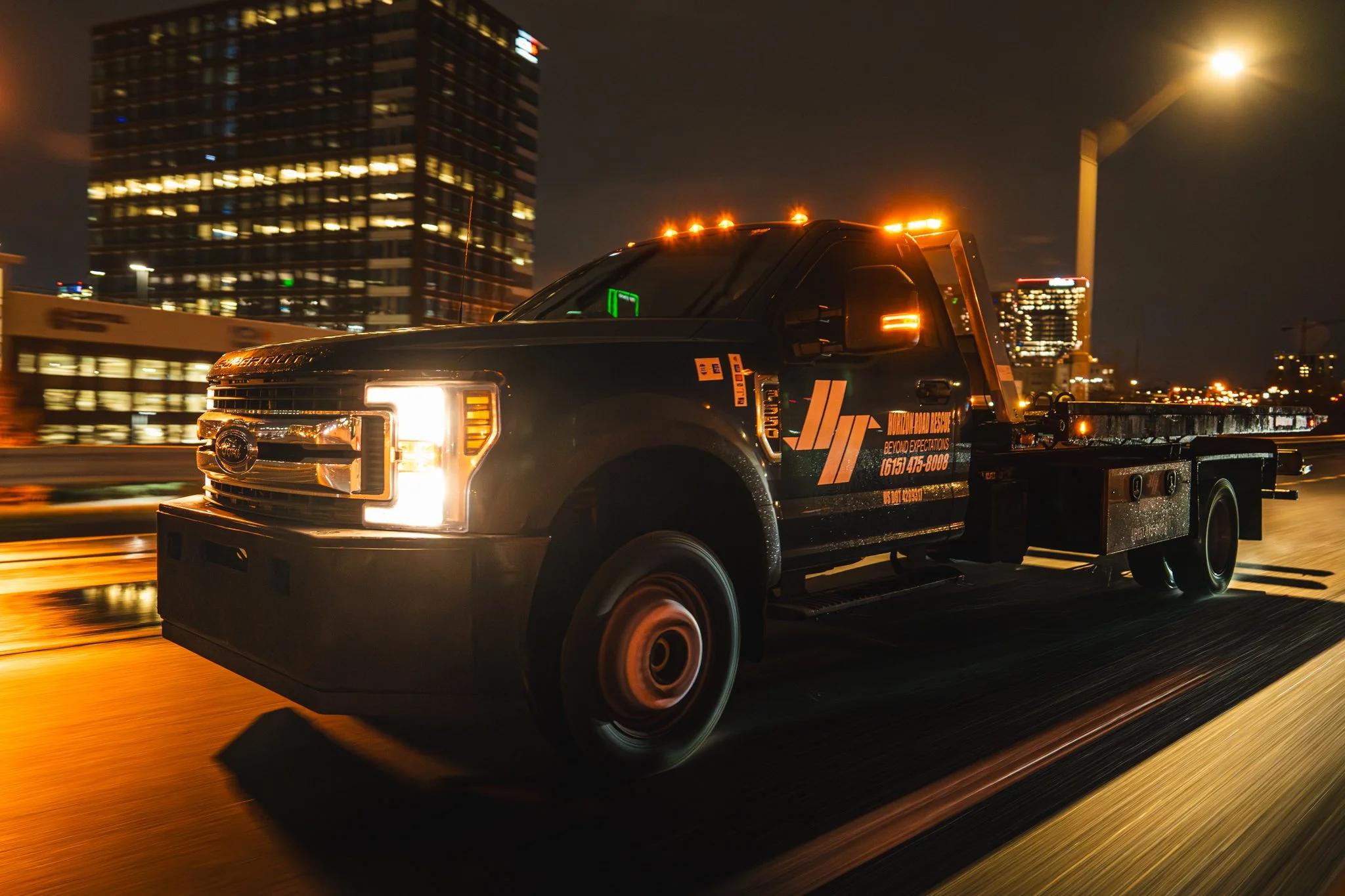 Tow truck driving at night with Nashville city lights in the background