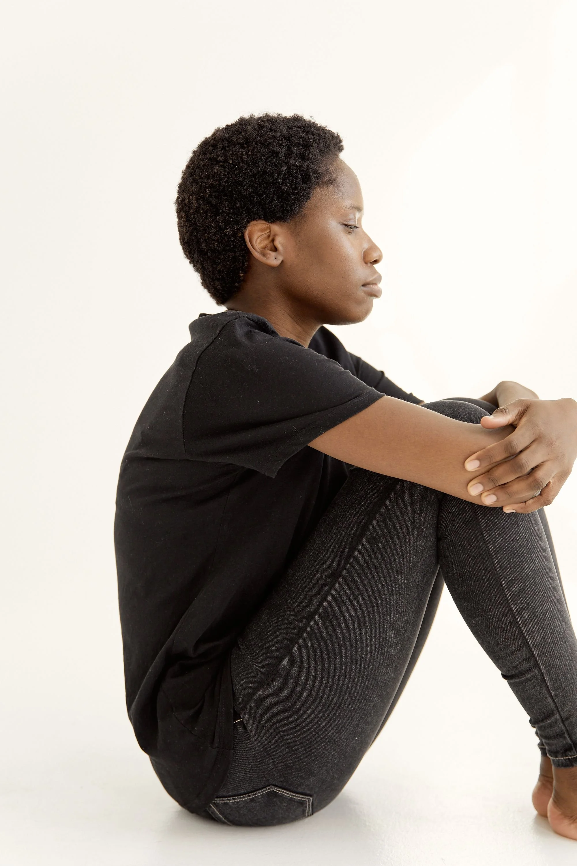Side profile of a woman sitting thoughtfully against a white background, conveying deep contemplation.