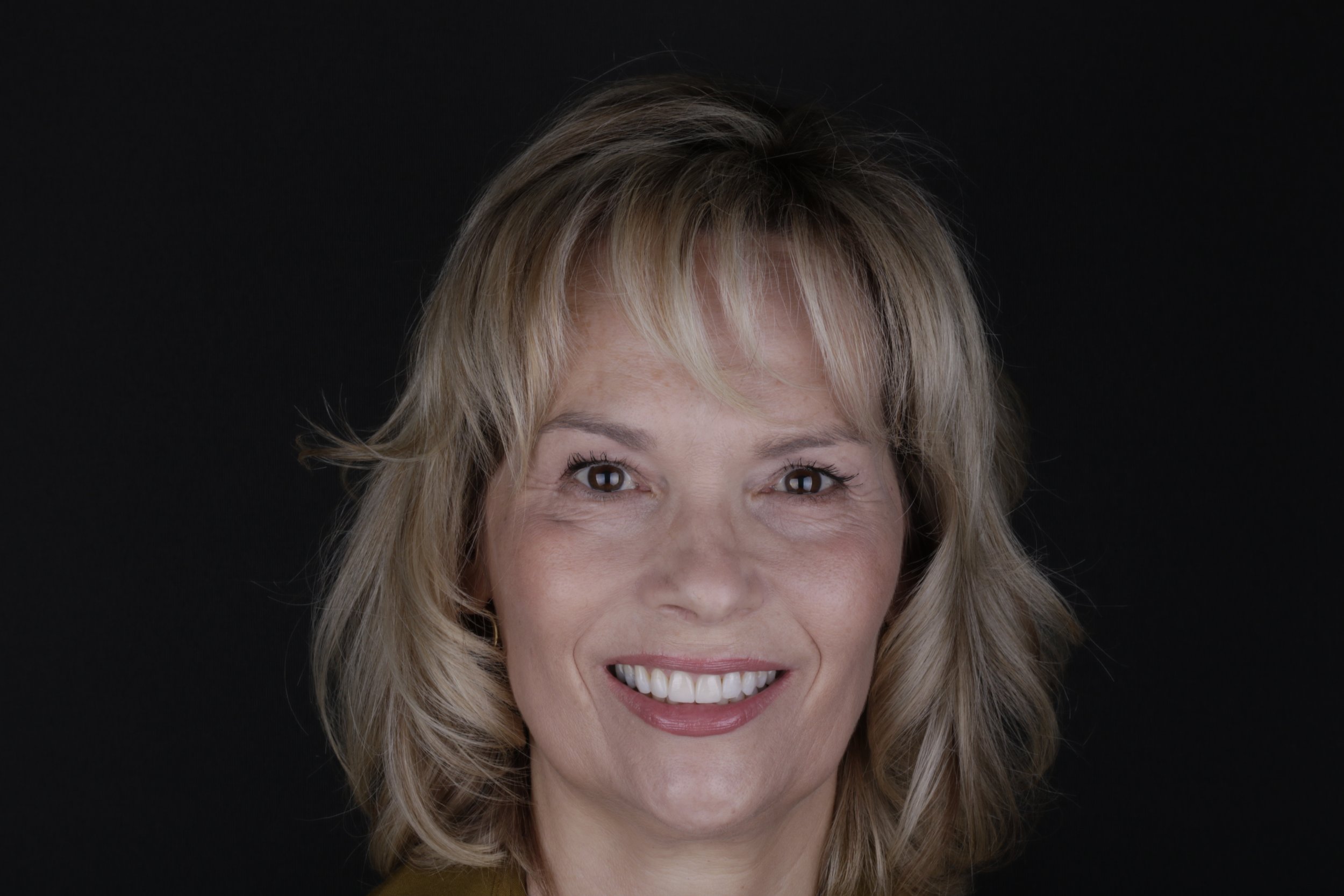 Close-up of smiling woman with blonde hair against black background.