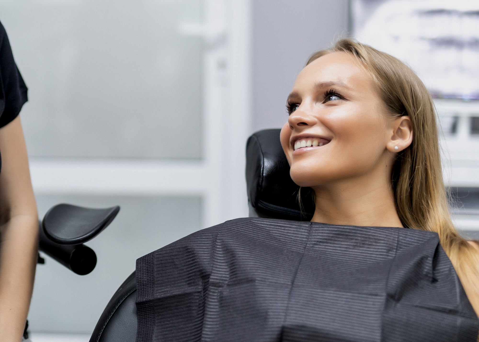 Close up of a young woman smiling in a black dental chair with a black dental bib