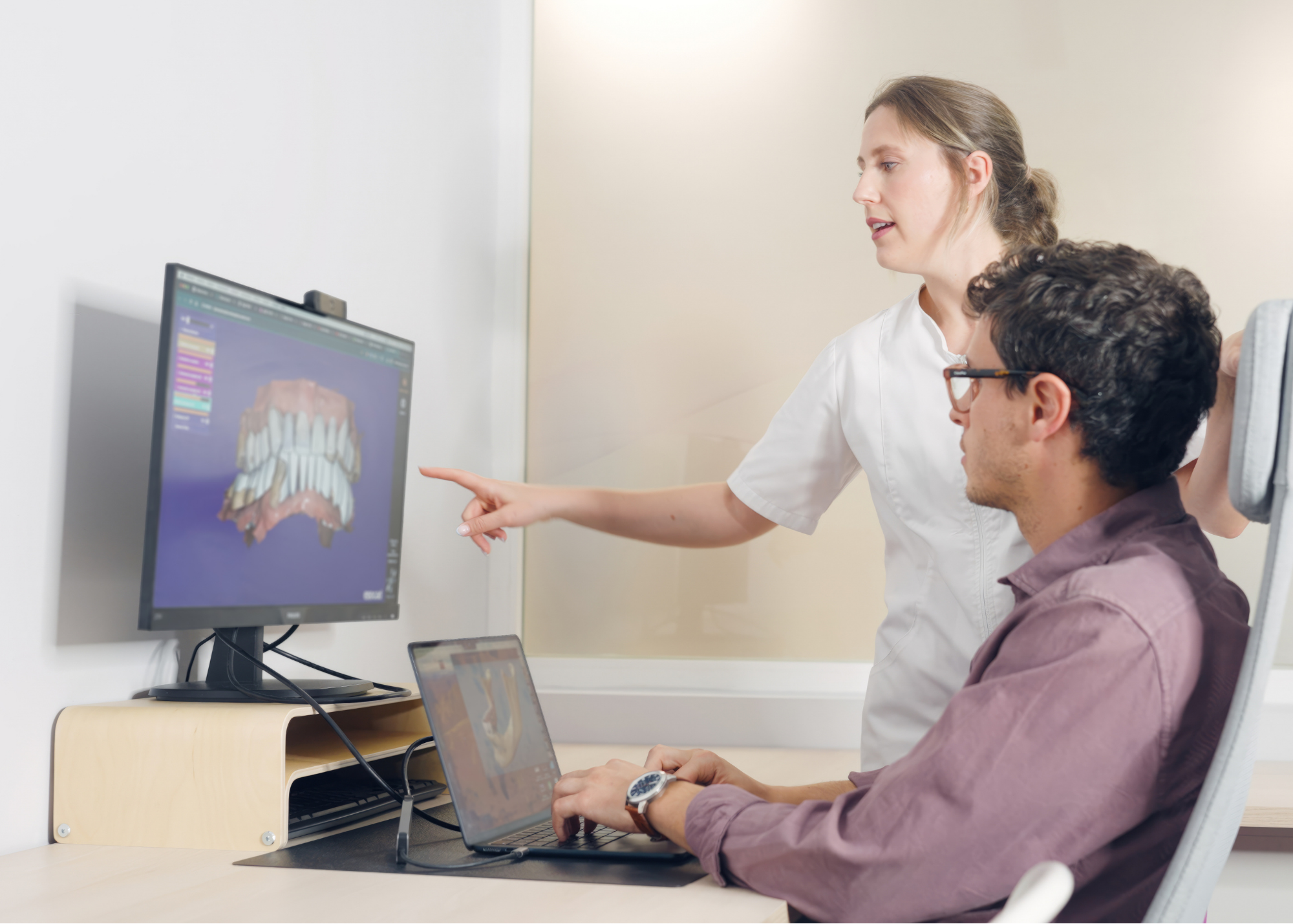 Medical professional explaining dental scan to male patient in an office, using a computer monitor displaying a 3D dental model.
