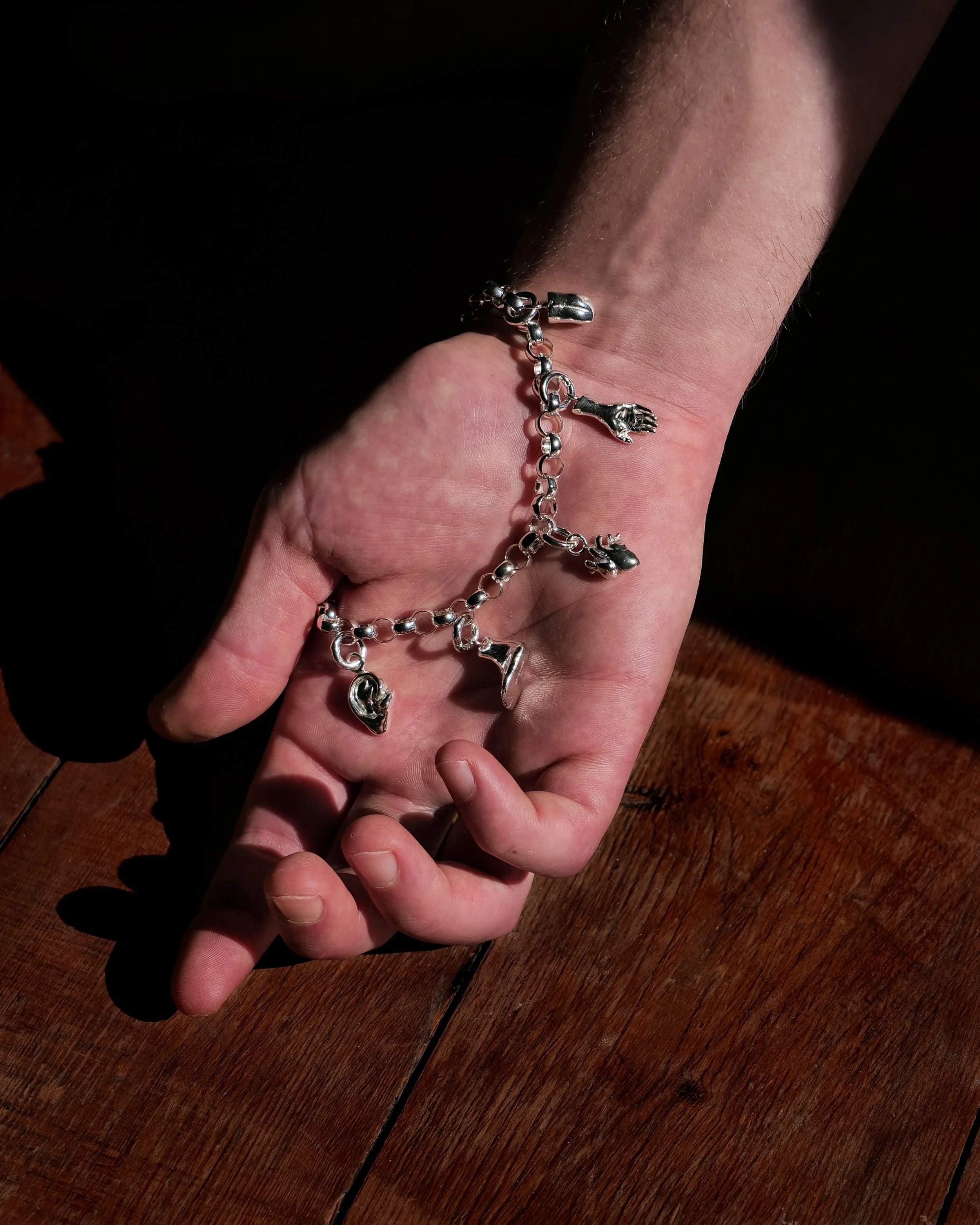 Close-up of a person wearing a sterling silver charm bracelet made up of body parts including an anatomical heart, foot, hand, tongue and ear.