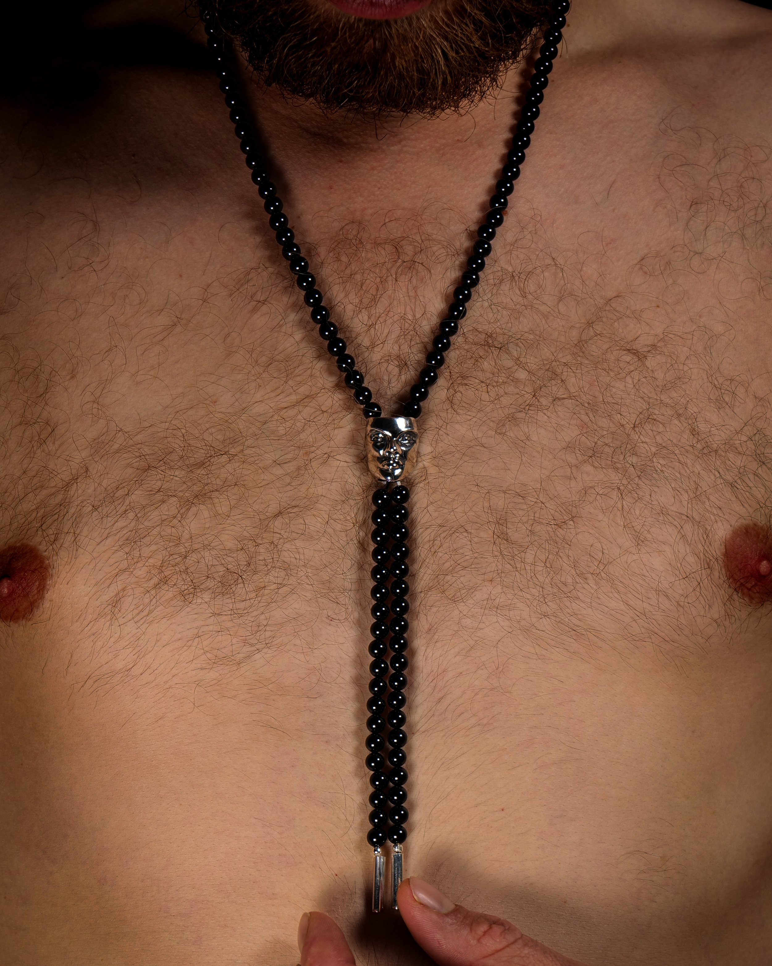 Close-up of a bolo tie necklace made from sterling silver and black tourmaline featuring a hand-sculpted face pendant.