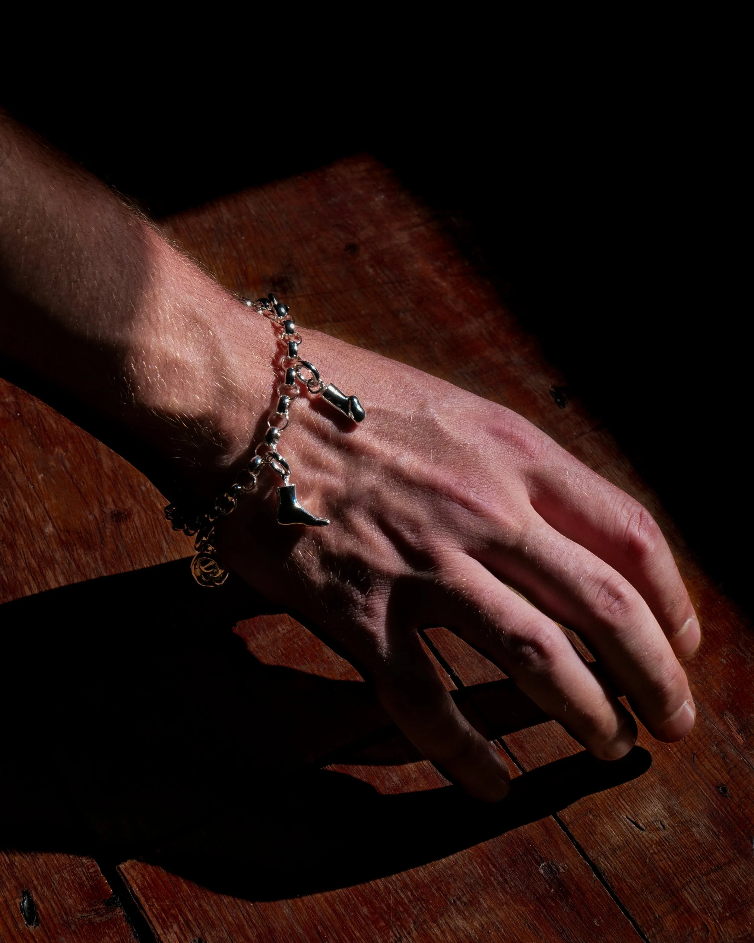 A hand wearing a sterling silver charm bracelet featuring body part charms