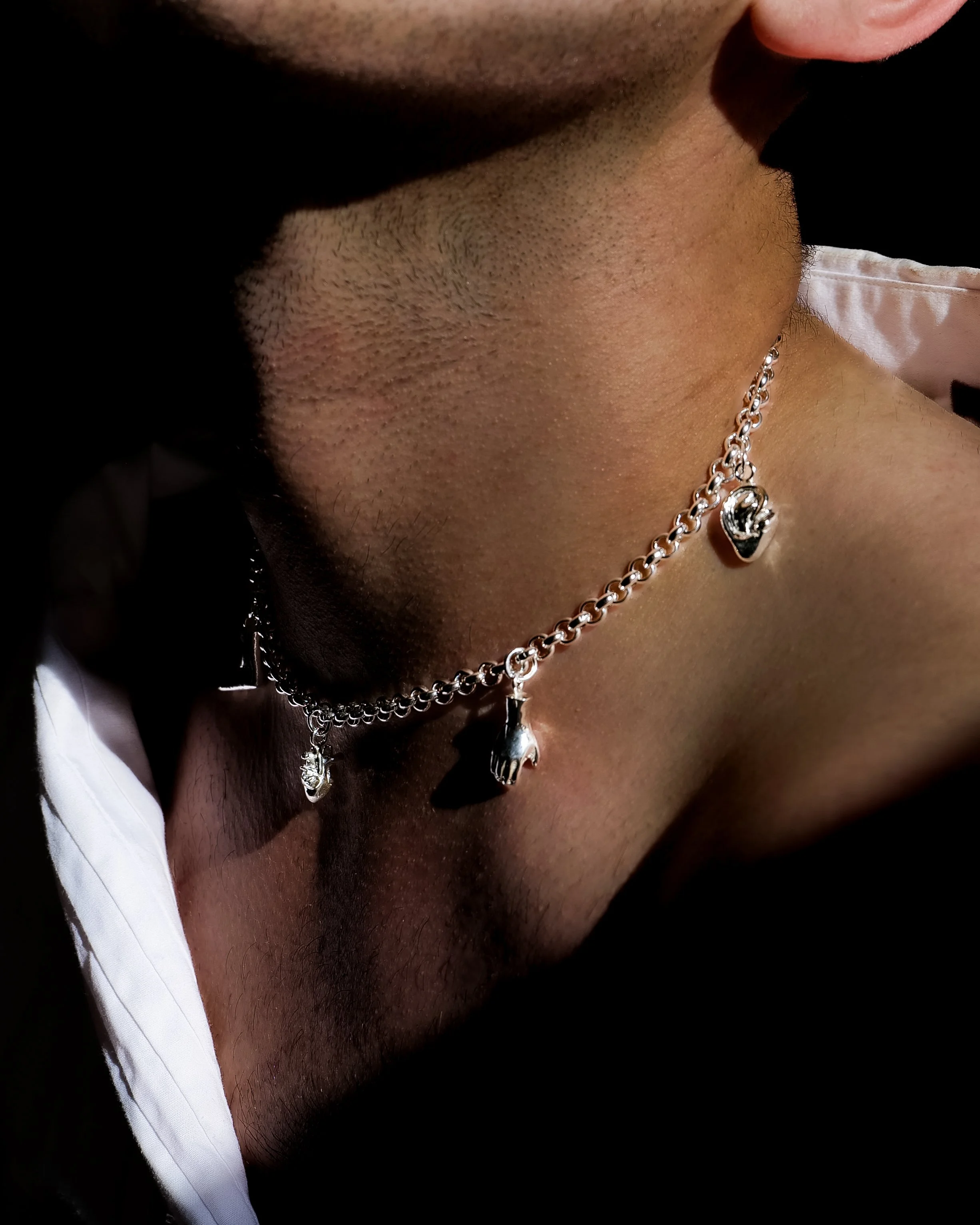 Close-up of a person's neck wearing a sterling silver charm chain made up of body parts, including a heart, hand and ear.