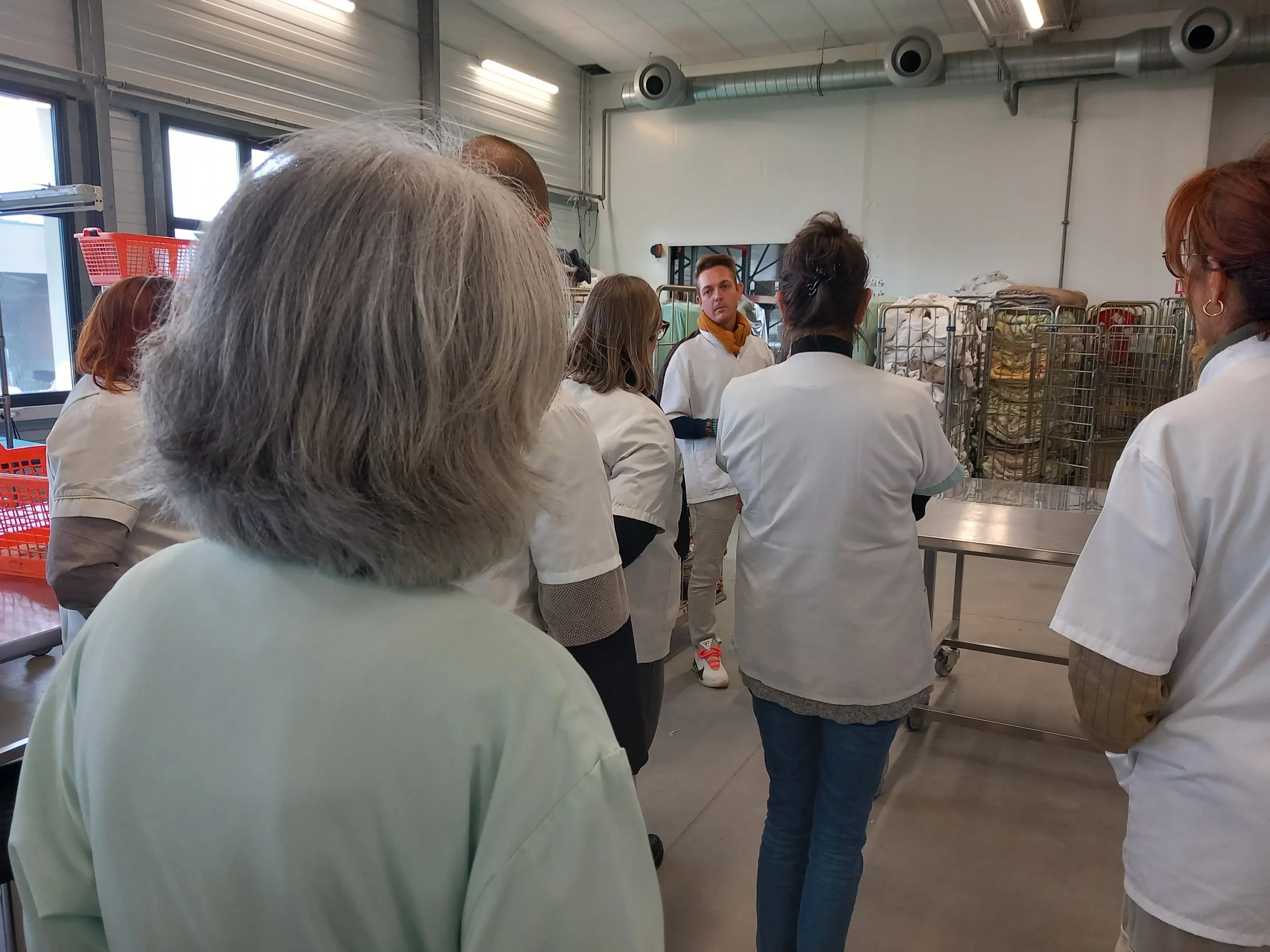 Groupe de personnes en blouse blanche dans un environnement industriel, probablement une salle de production ou de stockage.