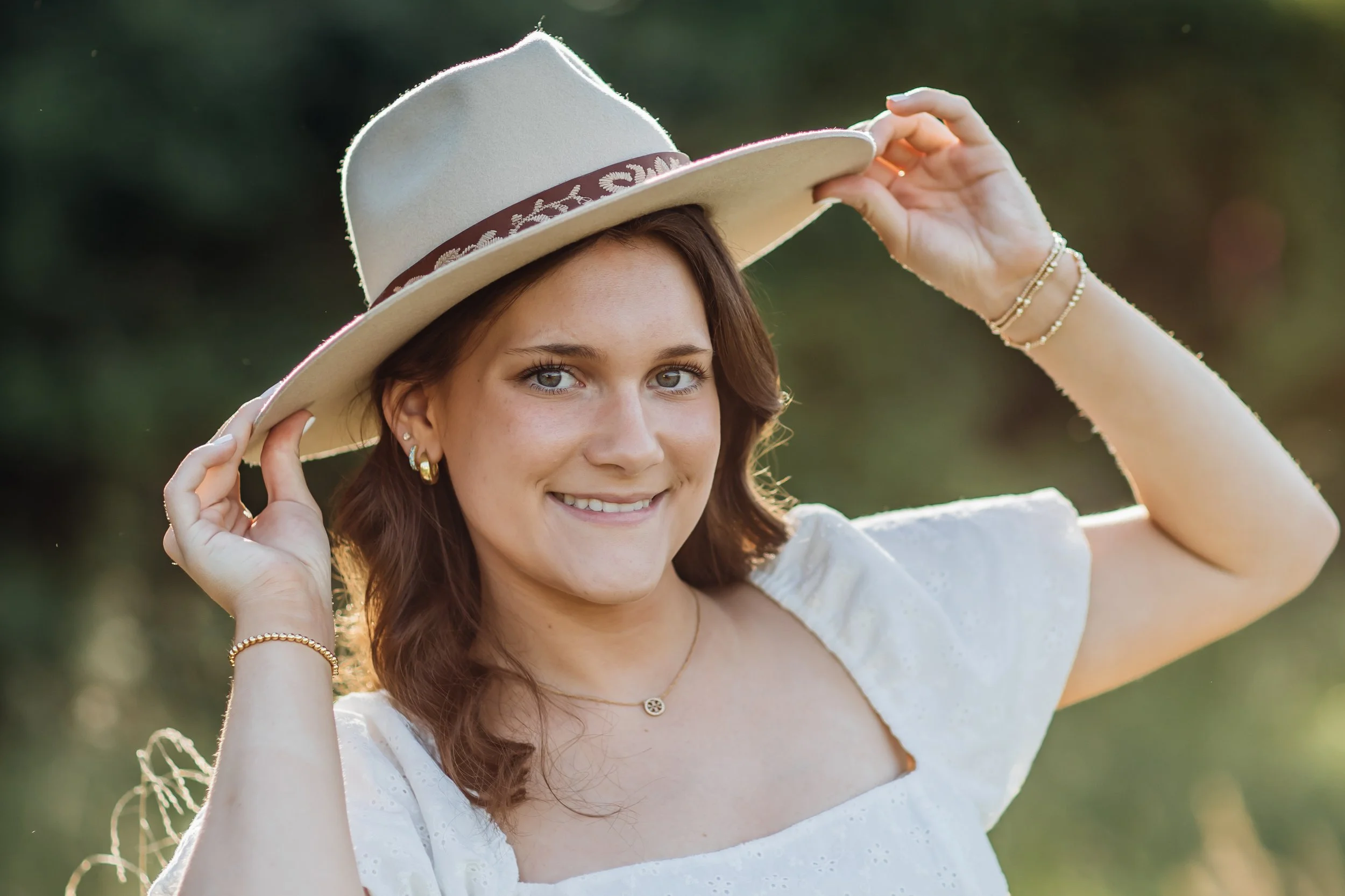 High School Senior posing with hands on hat in the sunshine