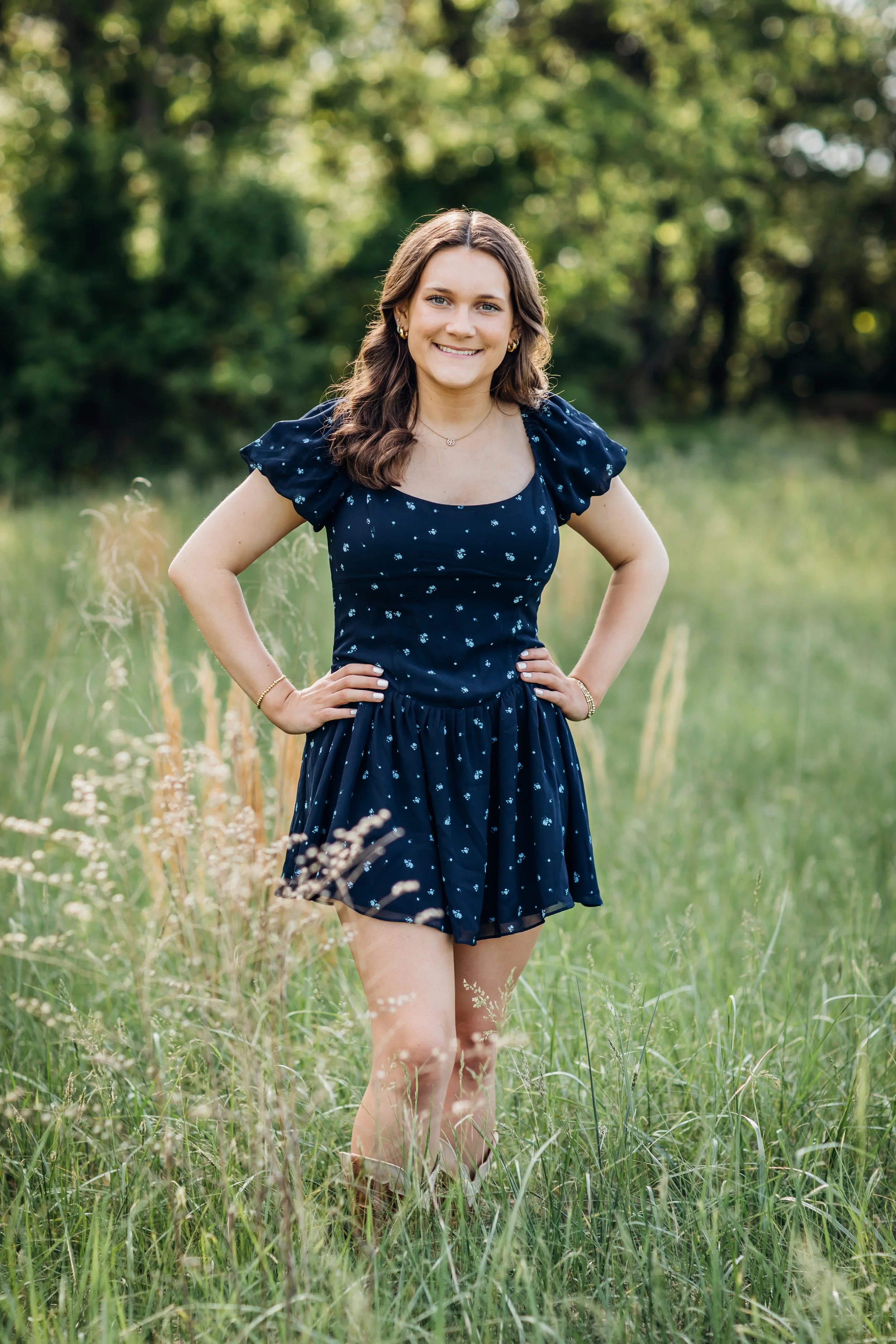 Senior girl posing with hands on hips in a field of high grass.