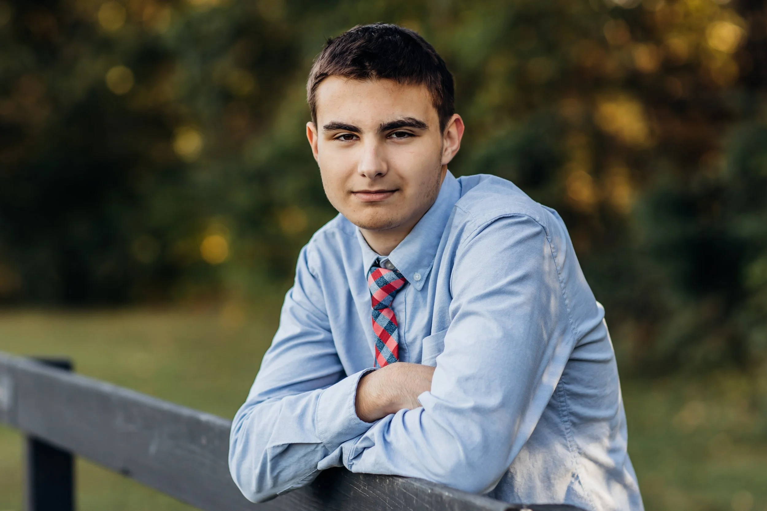 High School Senior with tie leans on fence