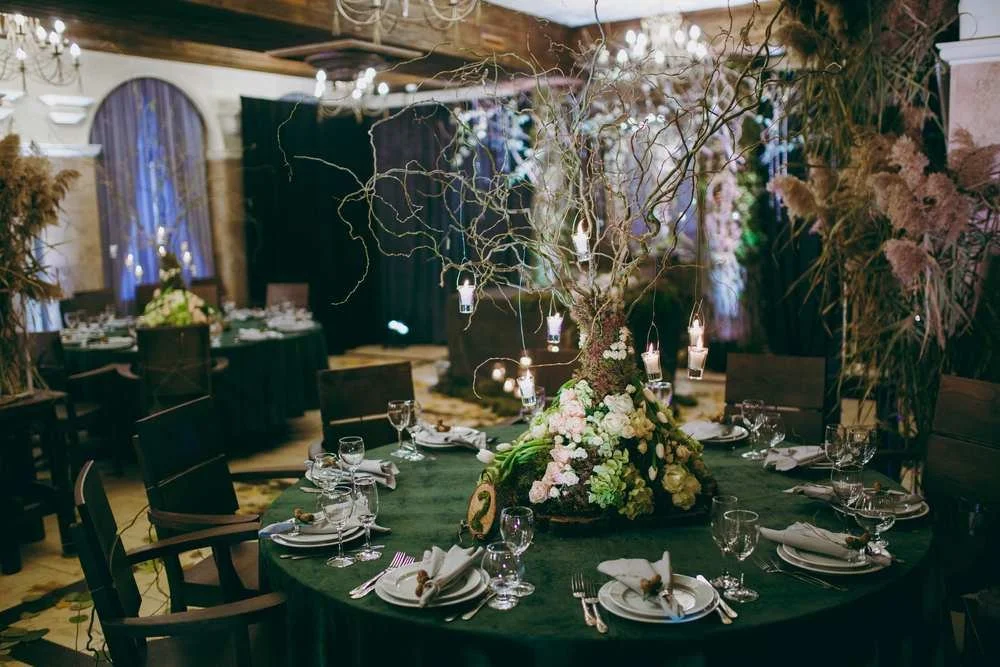 Spacious winter wedding reception table with deep green tablecloth, branch centrepiece, candles, and wide clearance for guests.