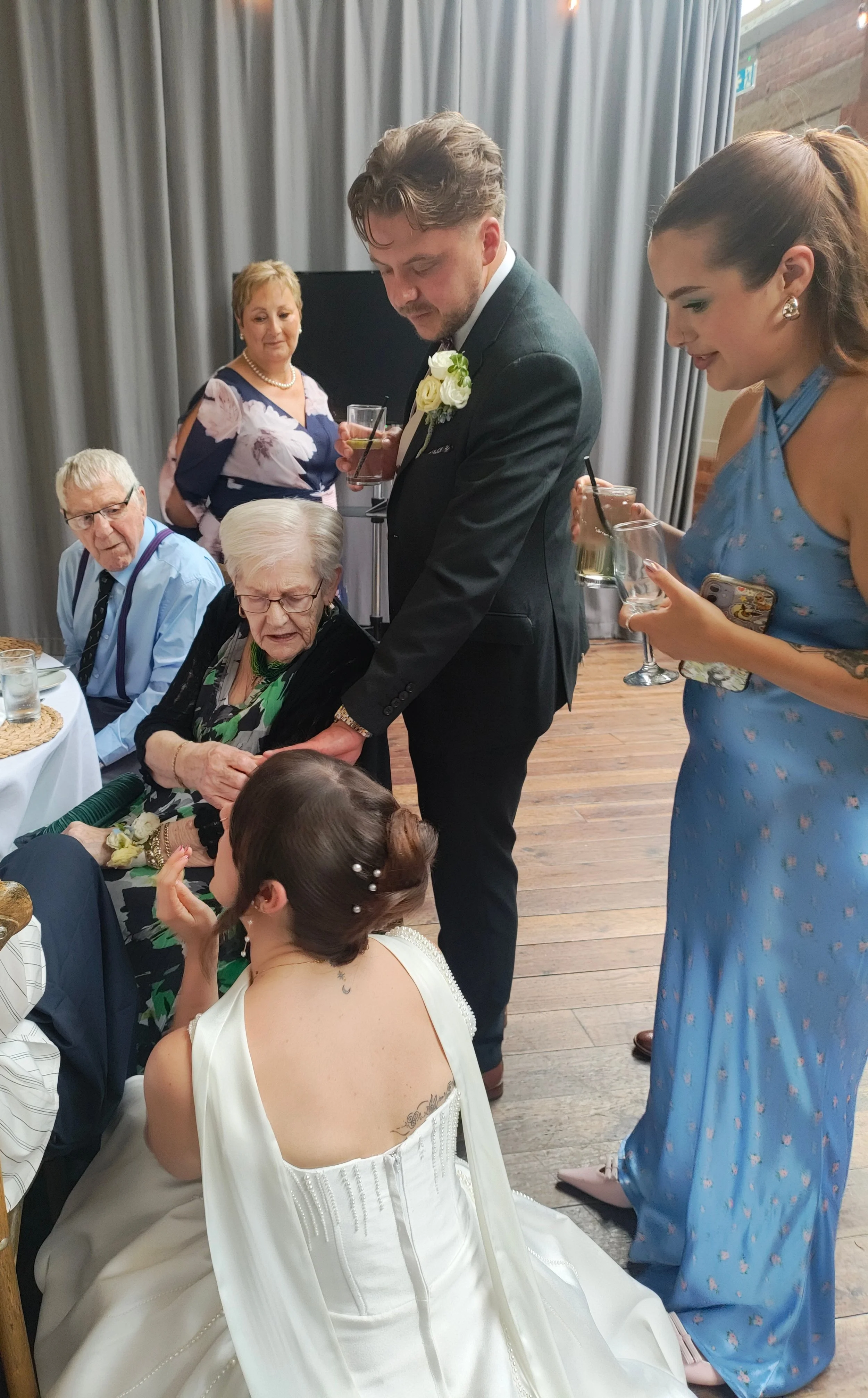 A bride with her grandparents at the wedding breakfast, both look confident and comfortable, enjoying the occassion