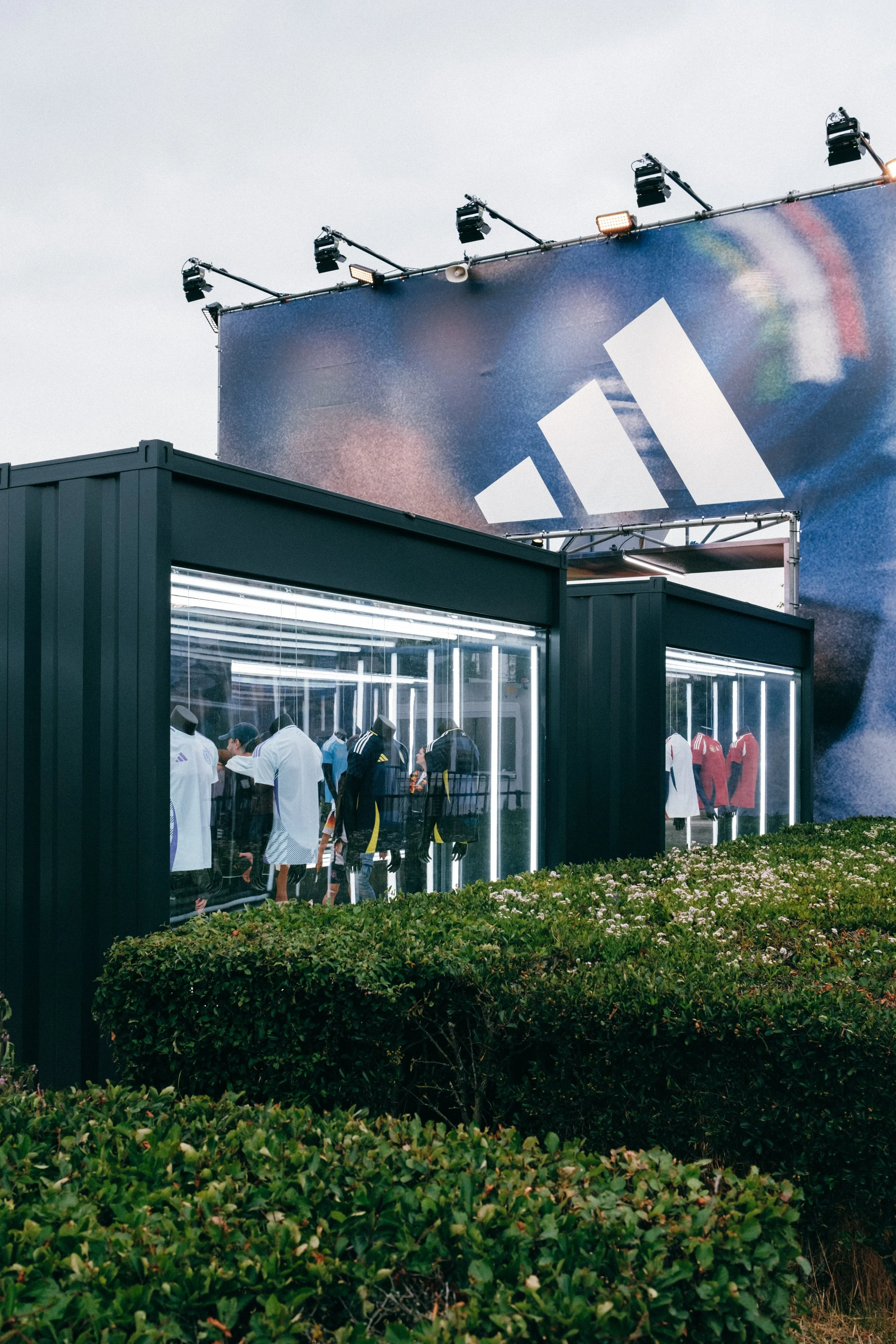 Modern outdoor display with Adidas billboard, mannequins in sportswear, and greenery.