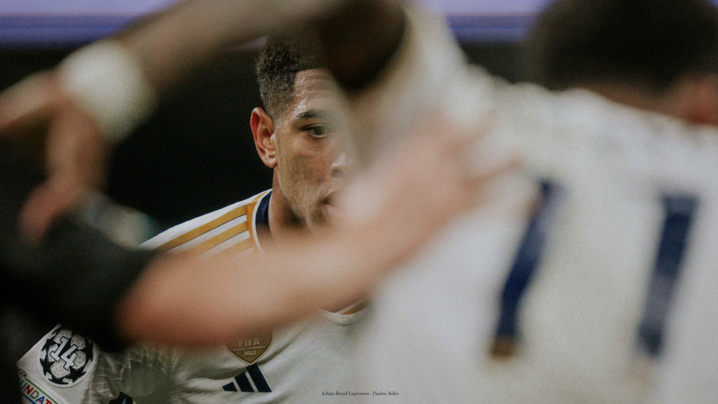 Soccer player partially obscured, wearing a white jersey with gold and blue accents, facing left.